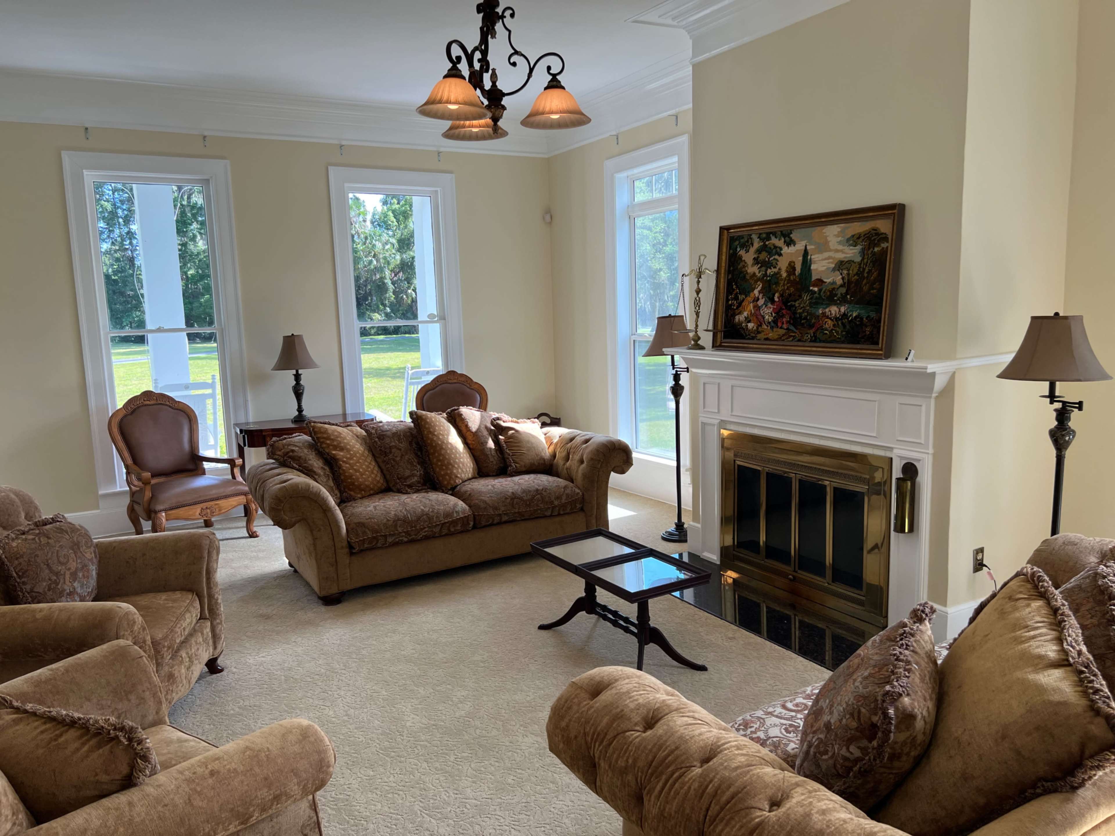 The living room features a beige sofa and armchairs arranged around a coffee table, with a decorative fireplace and large windows providing natural light.