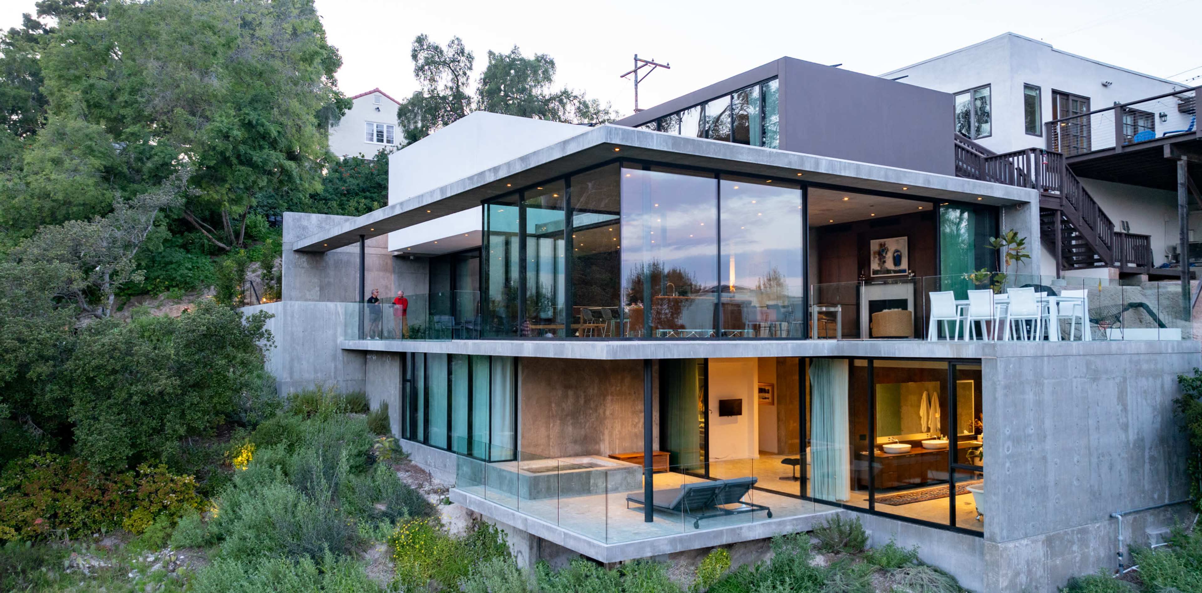 A modern house with extensive glass windows is built on a hillside, showcasing both outdoor landscaping and stylish interior spaces.