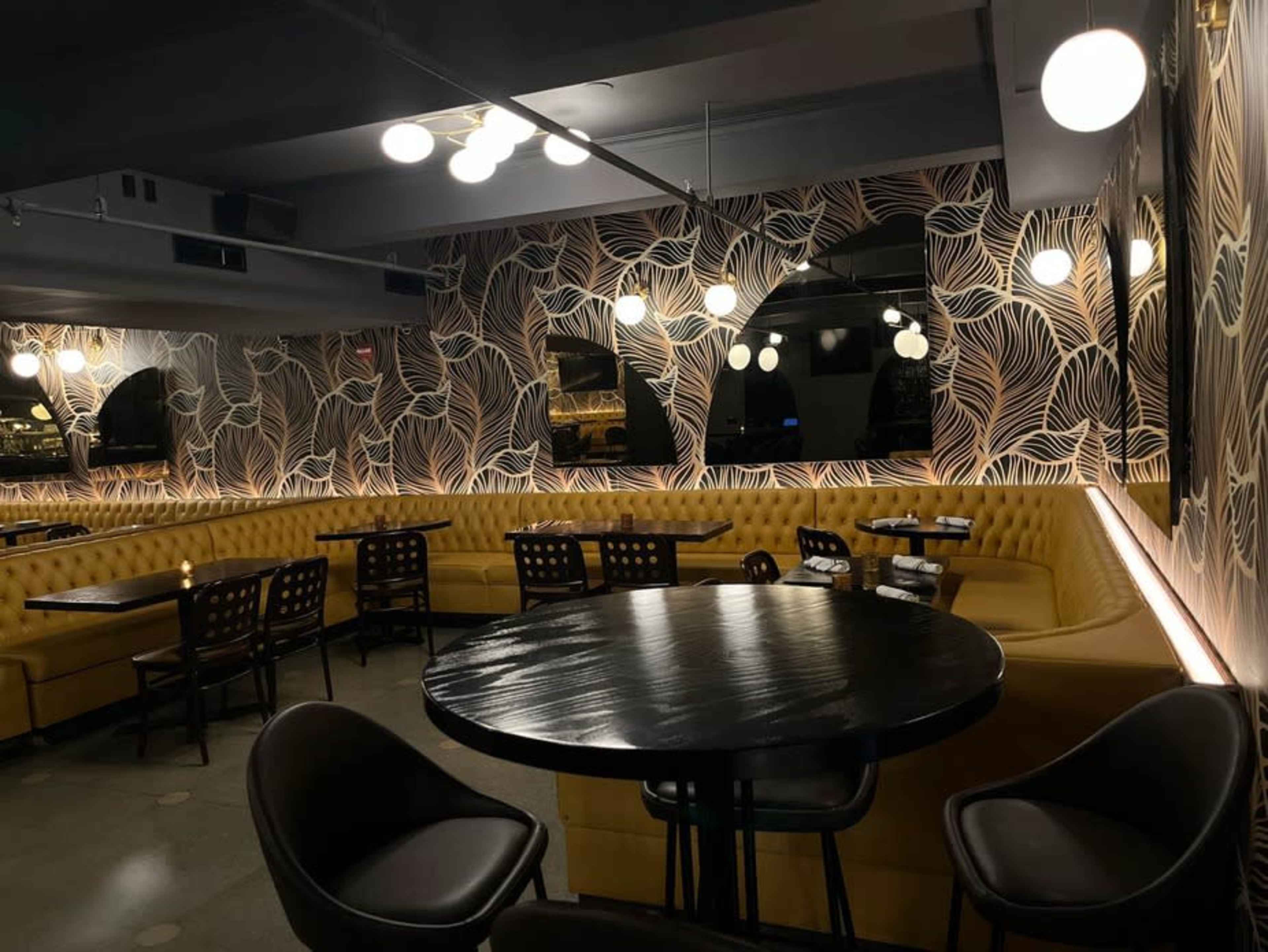 The image shows a modern restaurant interior with a yellow upholstered booth, round black tables, and decorative lighting.