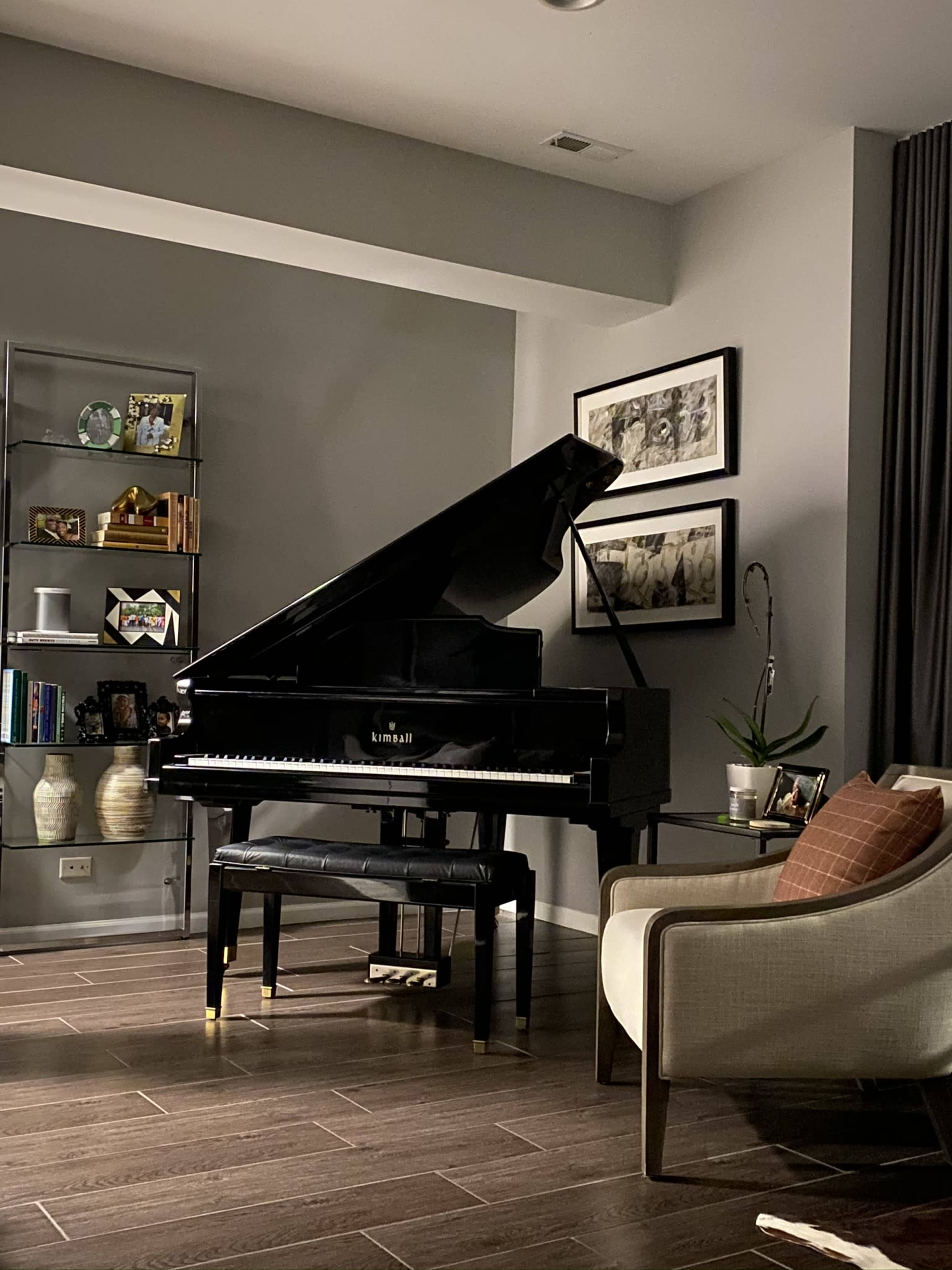 A black grand piano with its lid raised sits next to a modern armchair and a small table in a softly lit living room.