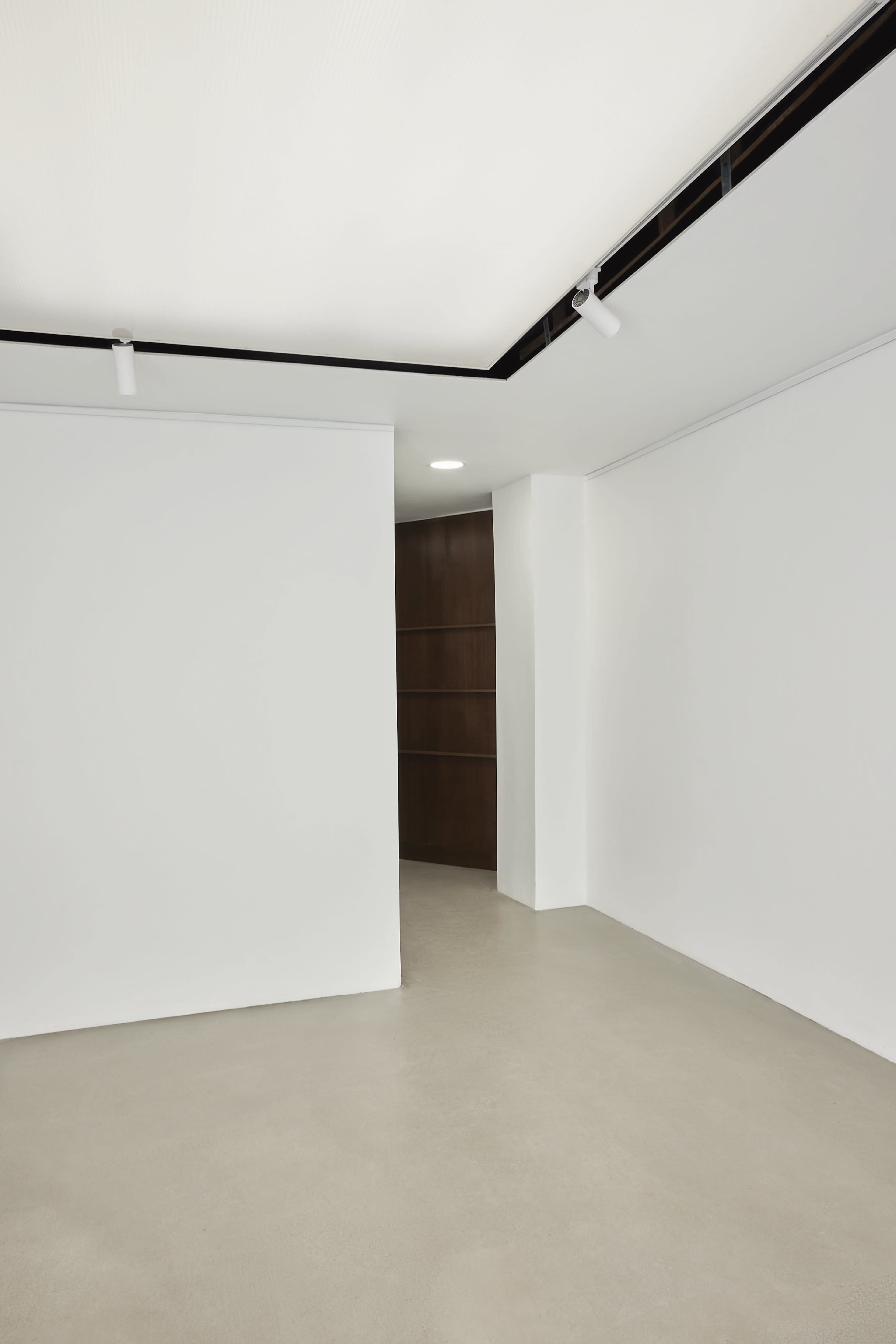 A minimalistic room features white walls and a smooth floor, with a doorway leading to another space.