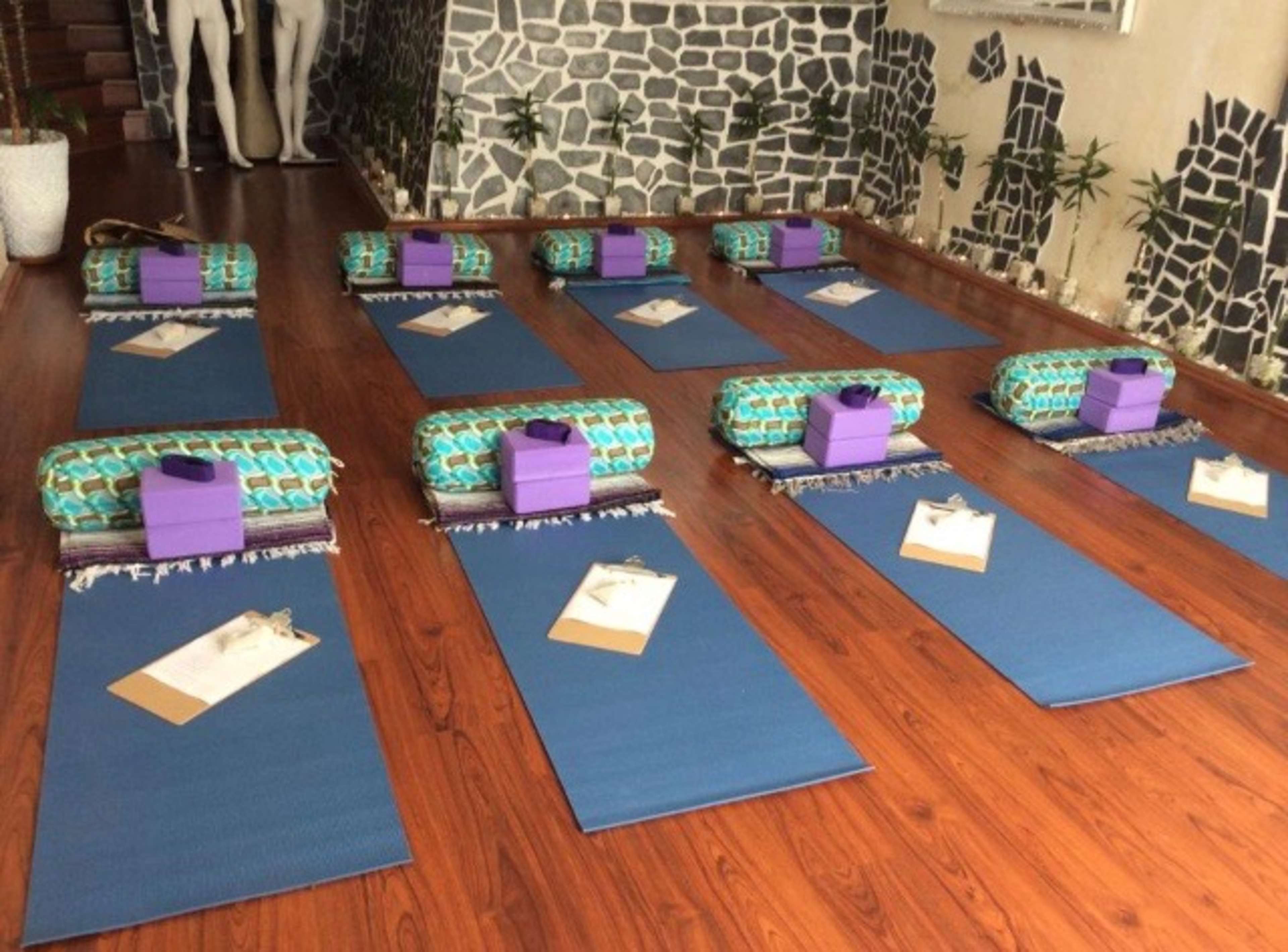The image shows a yoga studio with multiple exercise mats arranged in rows, each equipped with bolsters, props, and informational sheets.