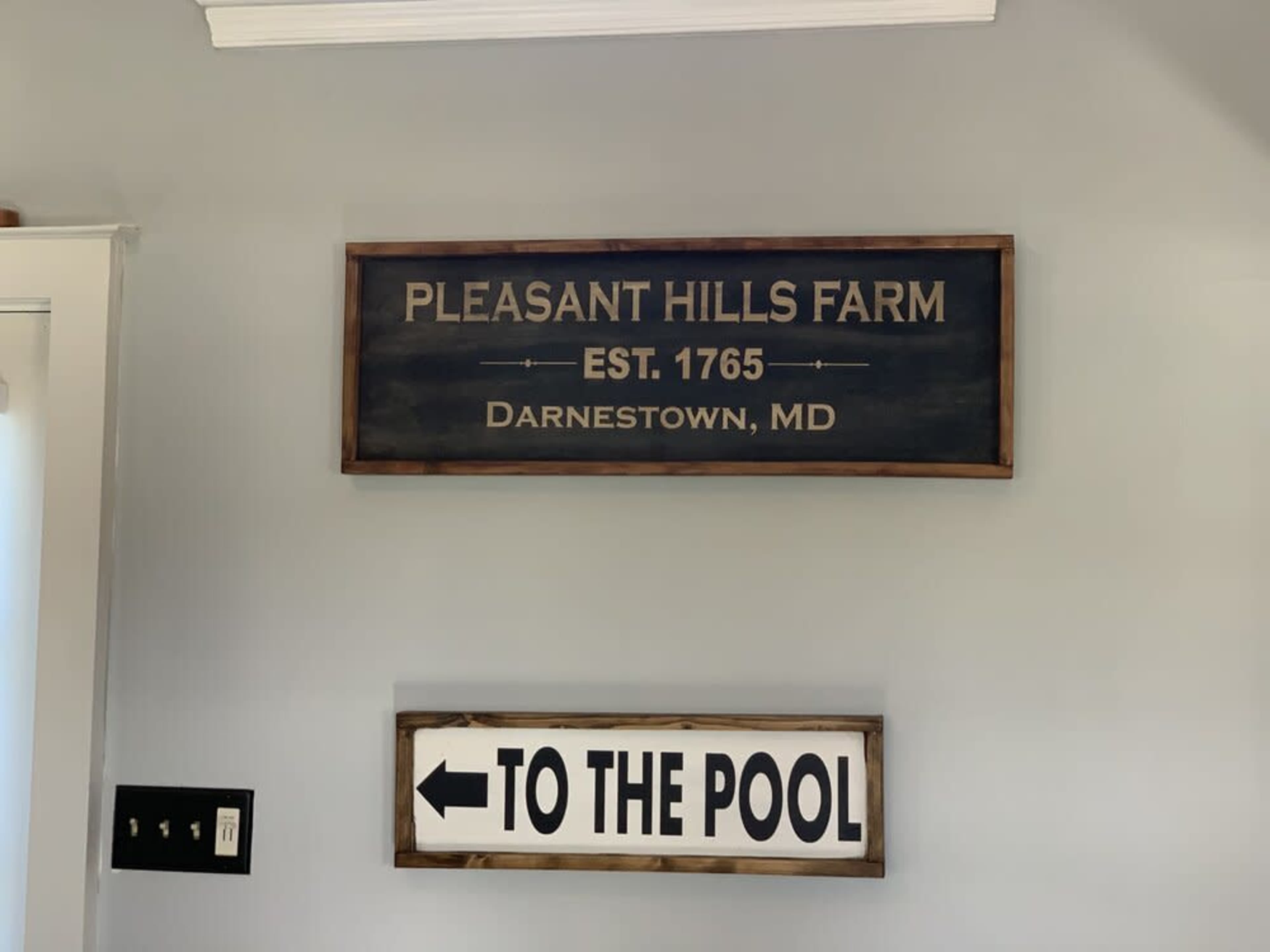Two signs on a wall, one identifying "Pleasant Hills Farm, Est. 1765, Darnestown, MD," and the other directing "To the Pool."