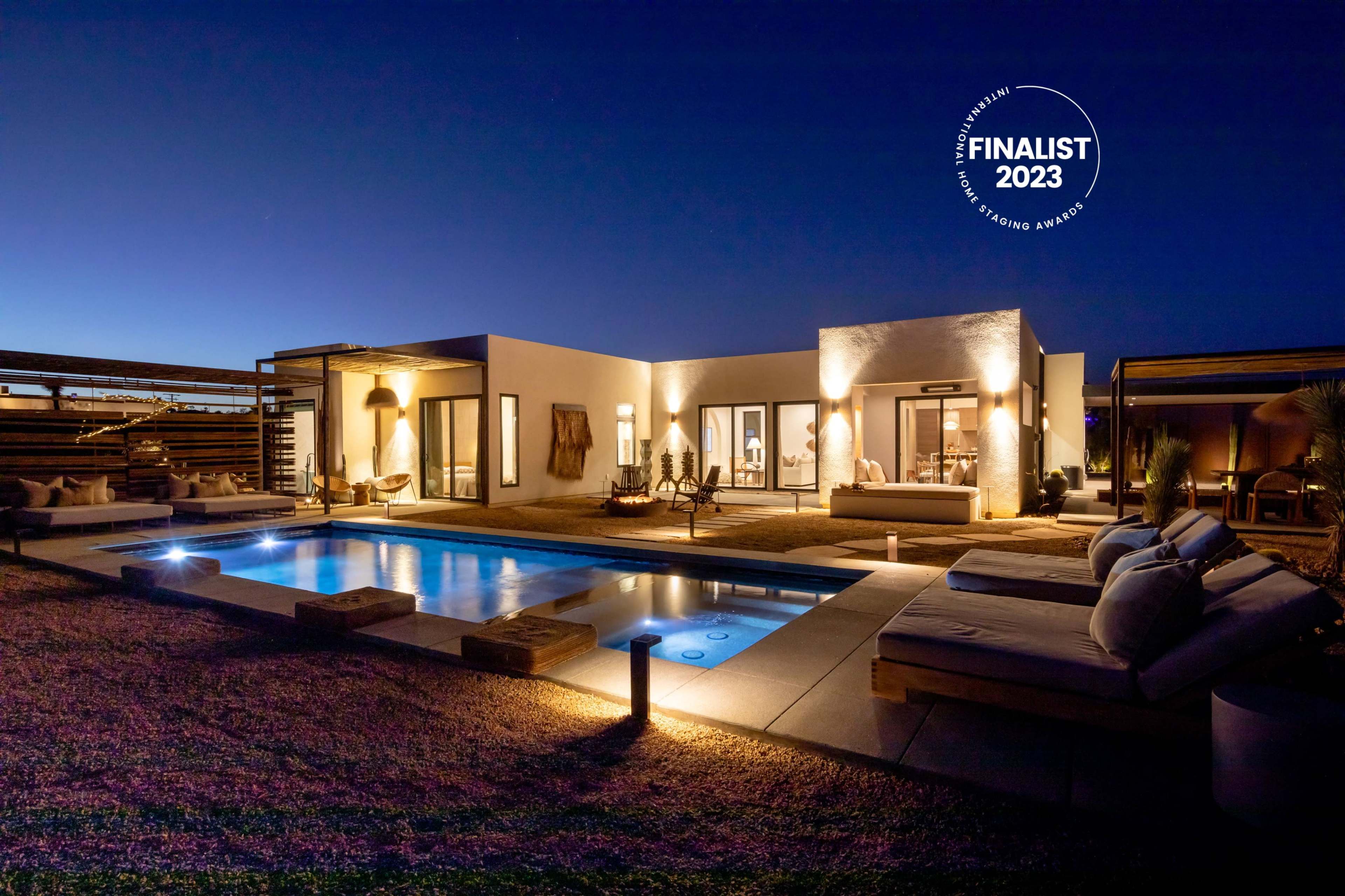 A modern villa with a pool and outdoor seating is illuminated at night, showcasing its design and ambiance.