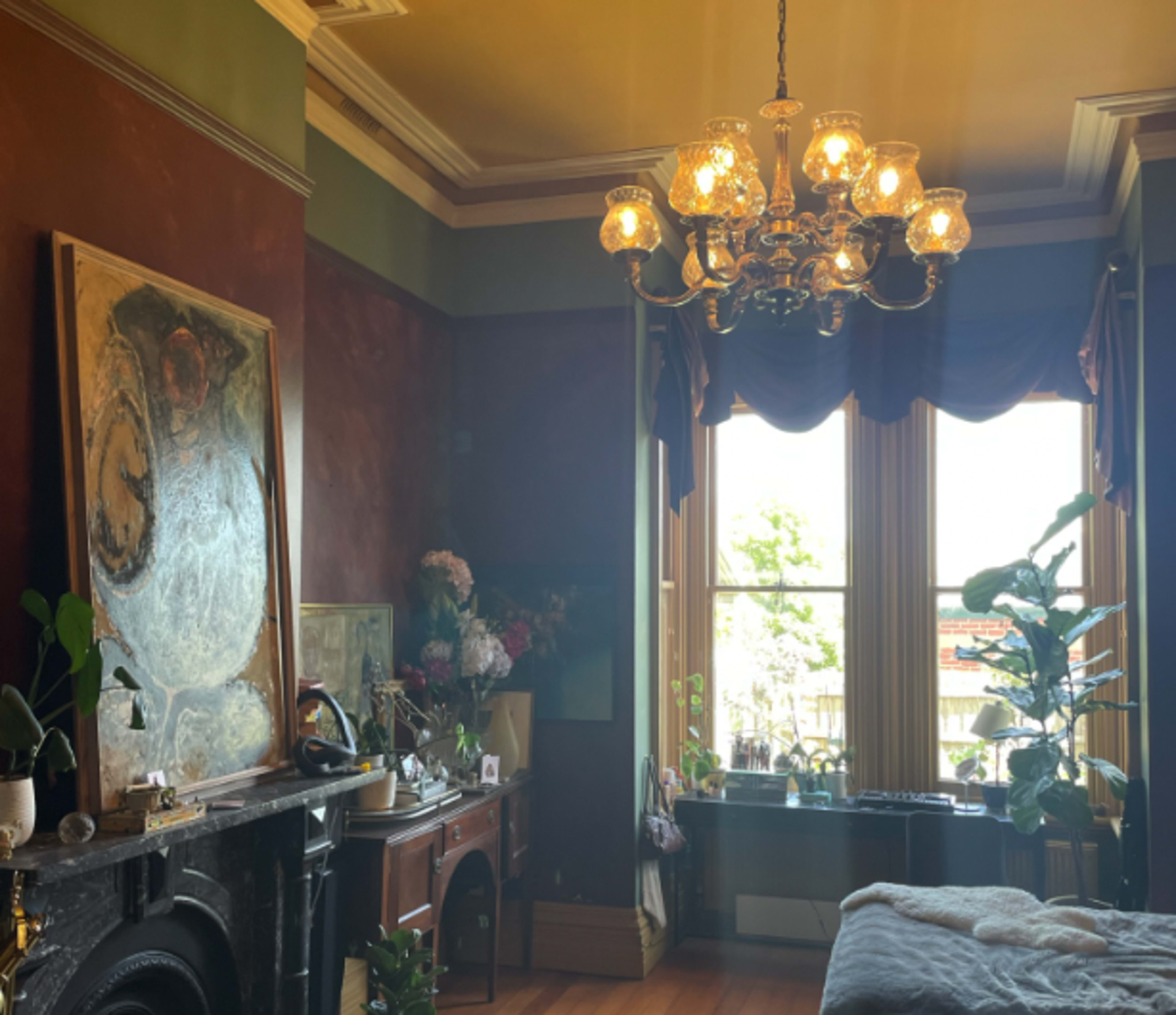 A well-lit room featuring a chandelier, large windows with drapes, a fireplace, and various plants and decorative items.