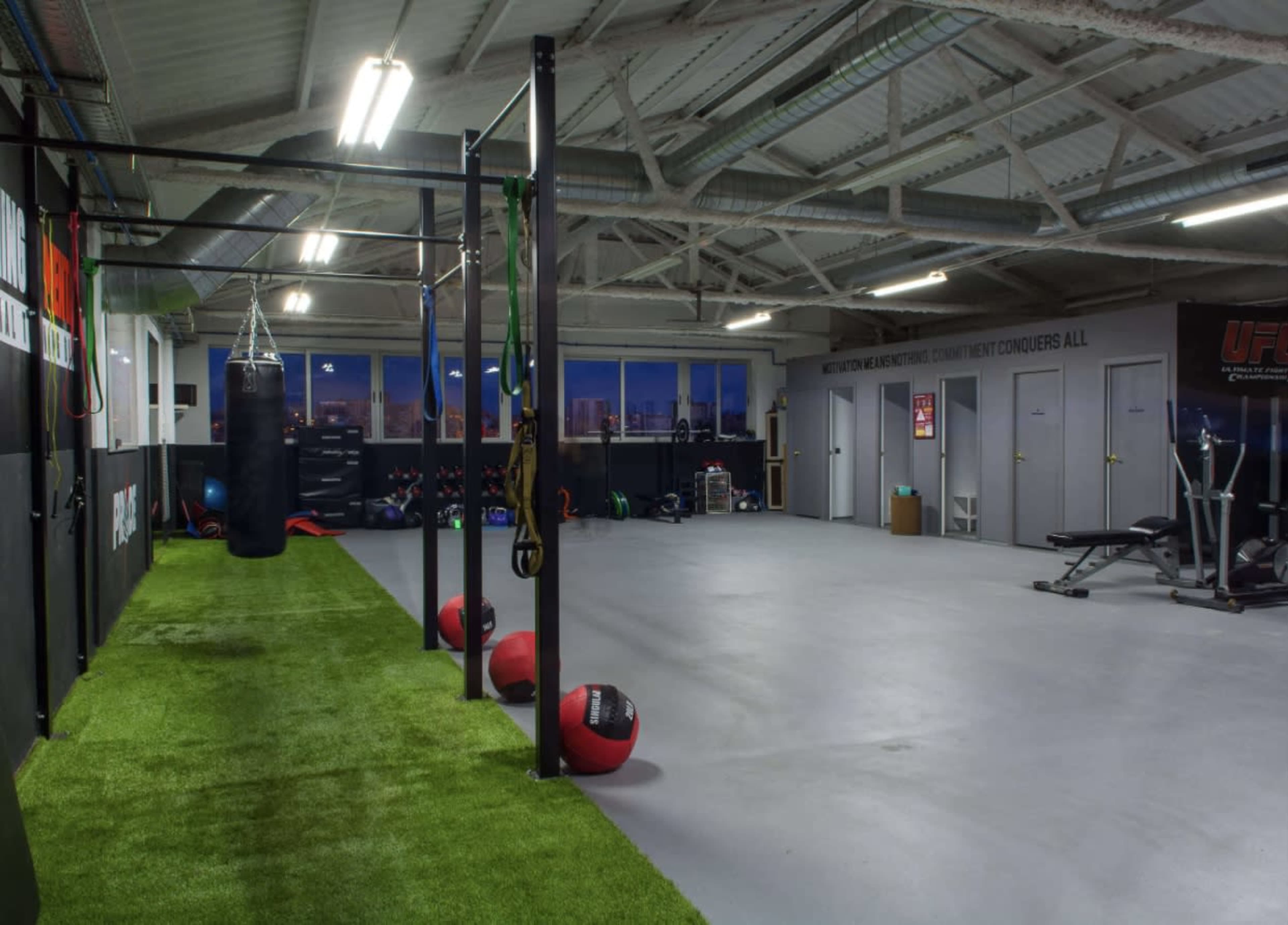 A spacious gym with exercise equipment, boxing bags, and a green turf area.