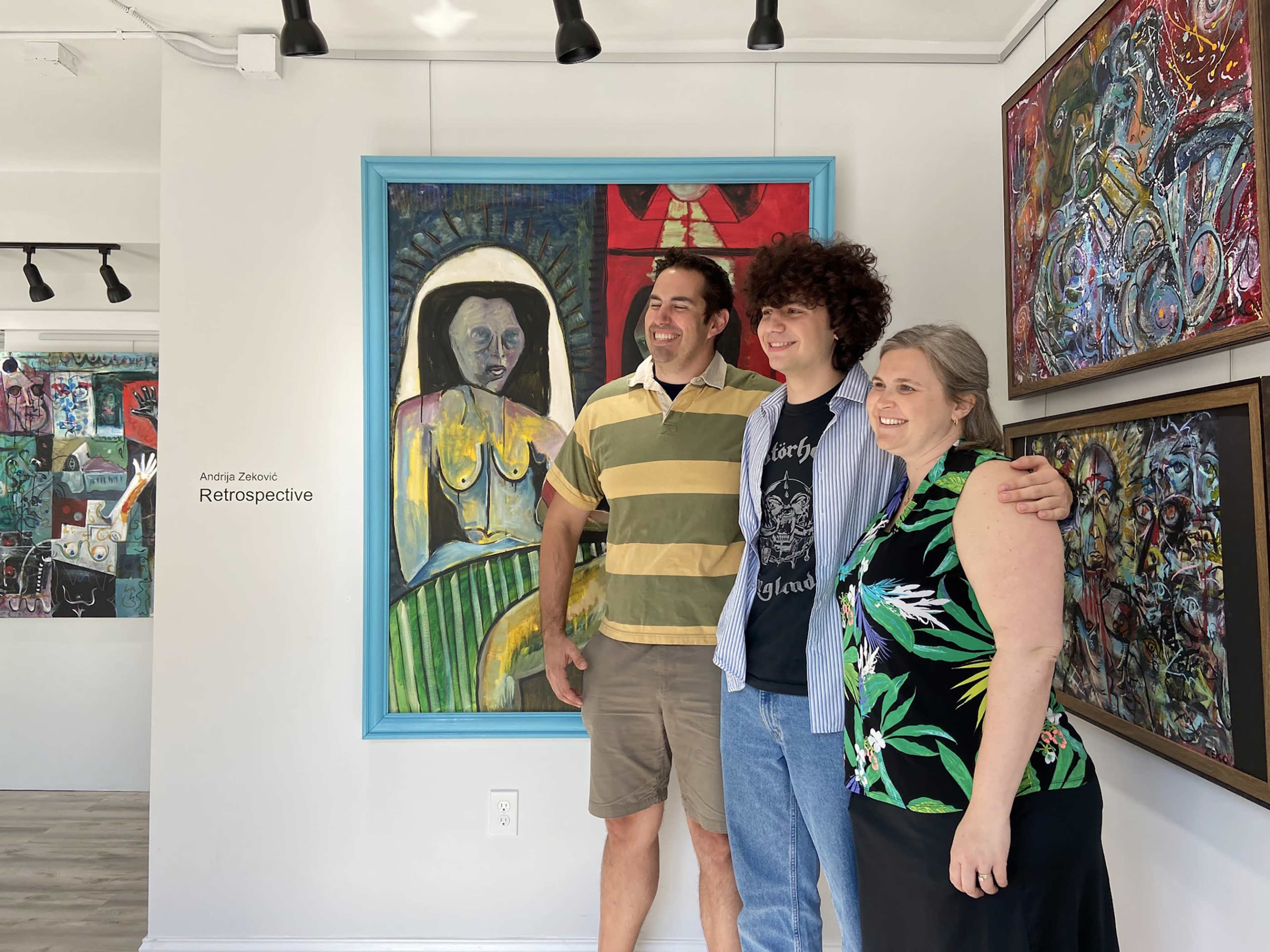 Three people pose for a photo in an art gallery featuring vibrant paintings on the walls.