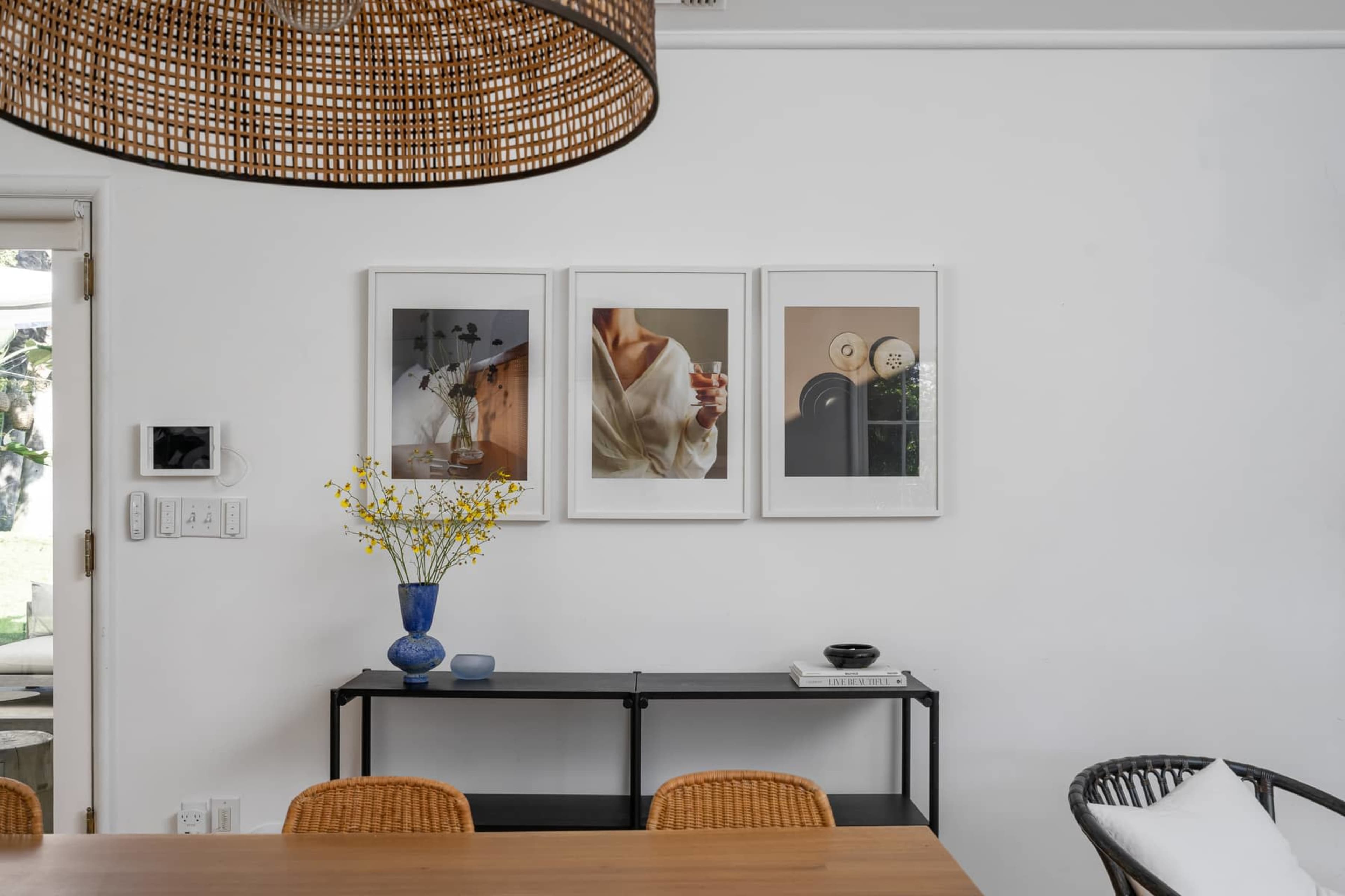A dining area features a table, a black shelving unit with decorative items, and three framed photographs displayed on the wall above.
