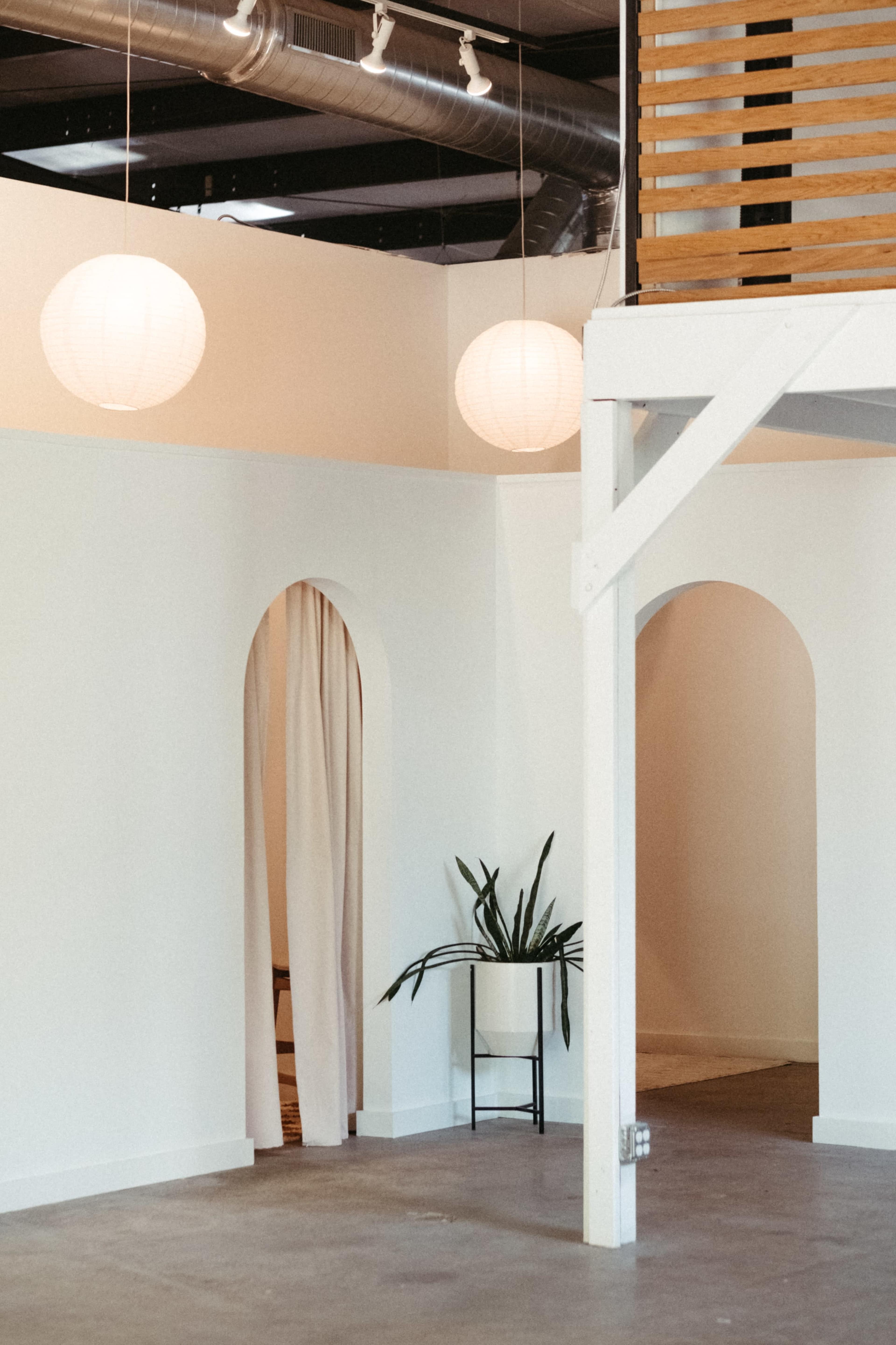 The image shows a light-filled interior space with white walls, a potted plant on a small table, and large paper lanterns hanging from the ceiling.
