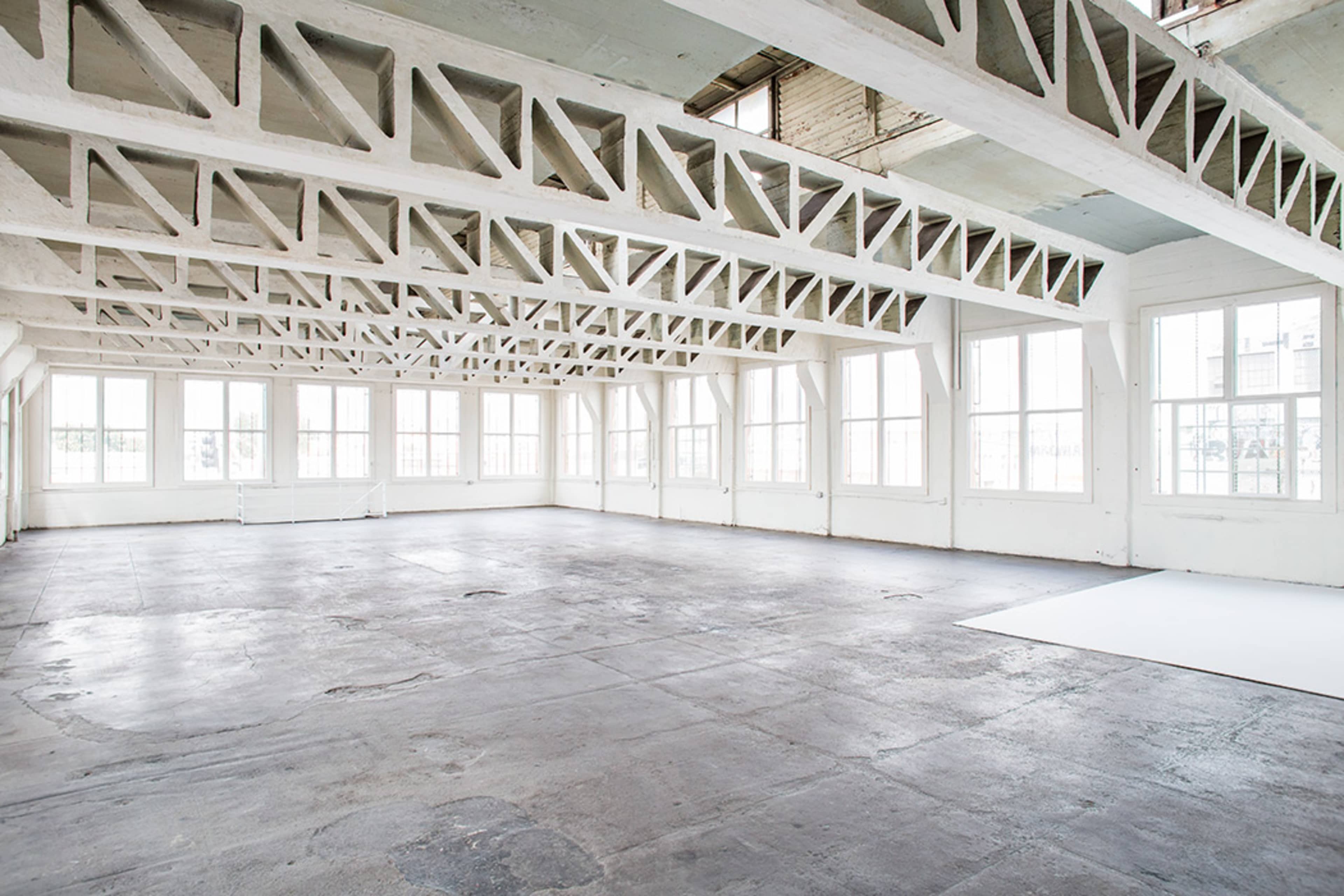A spacious, empty industrial room with large windows and exposed beam structures.