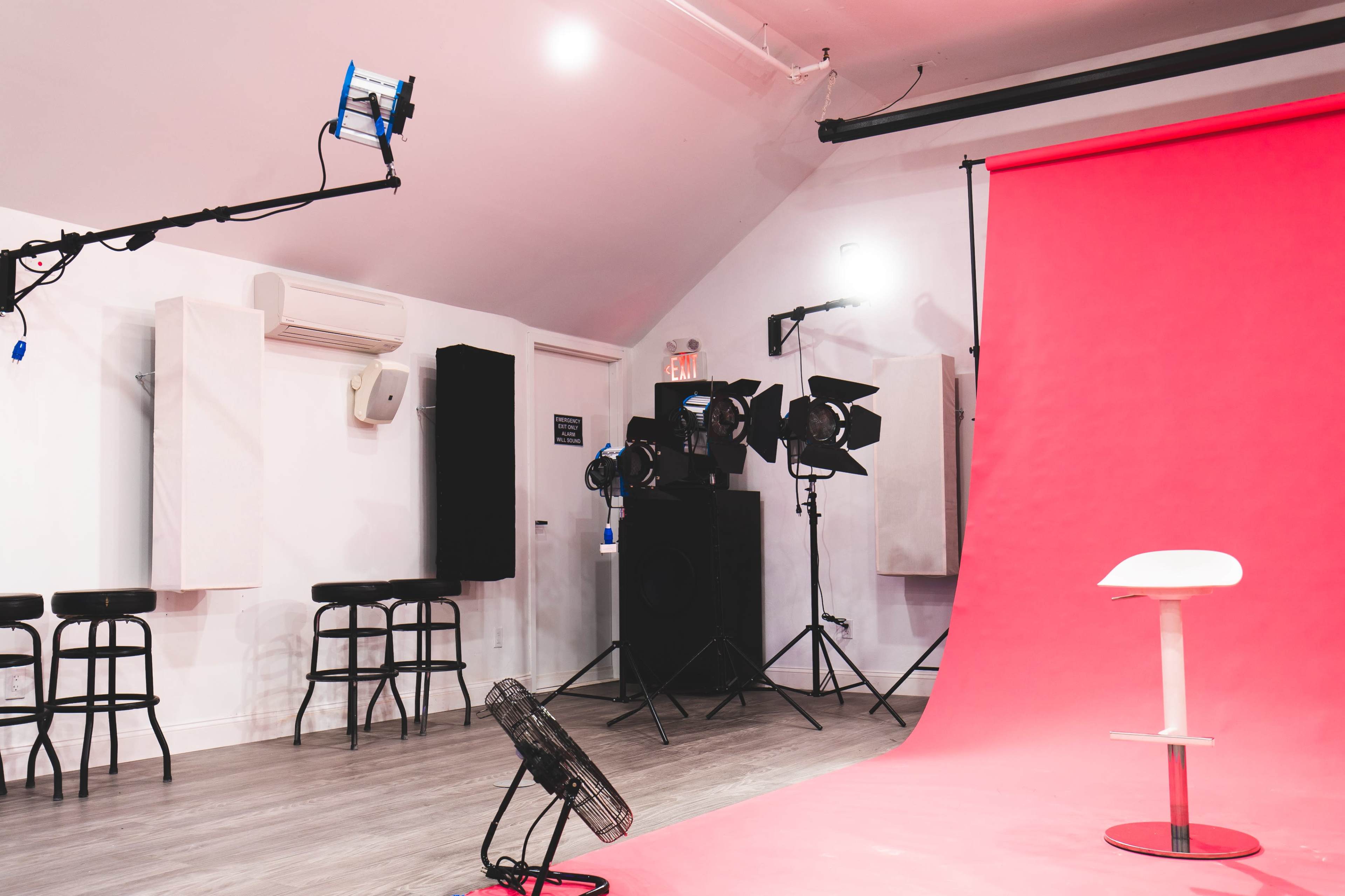 This image features a photo studio with a pink backdrop, studio lights, and a white chair in front of it.