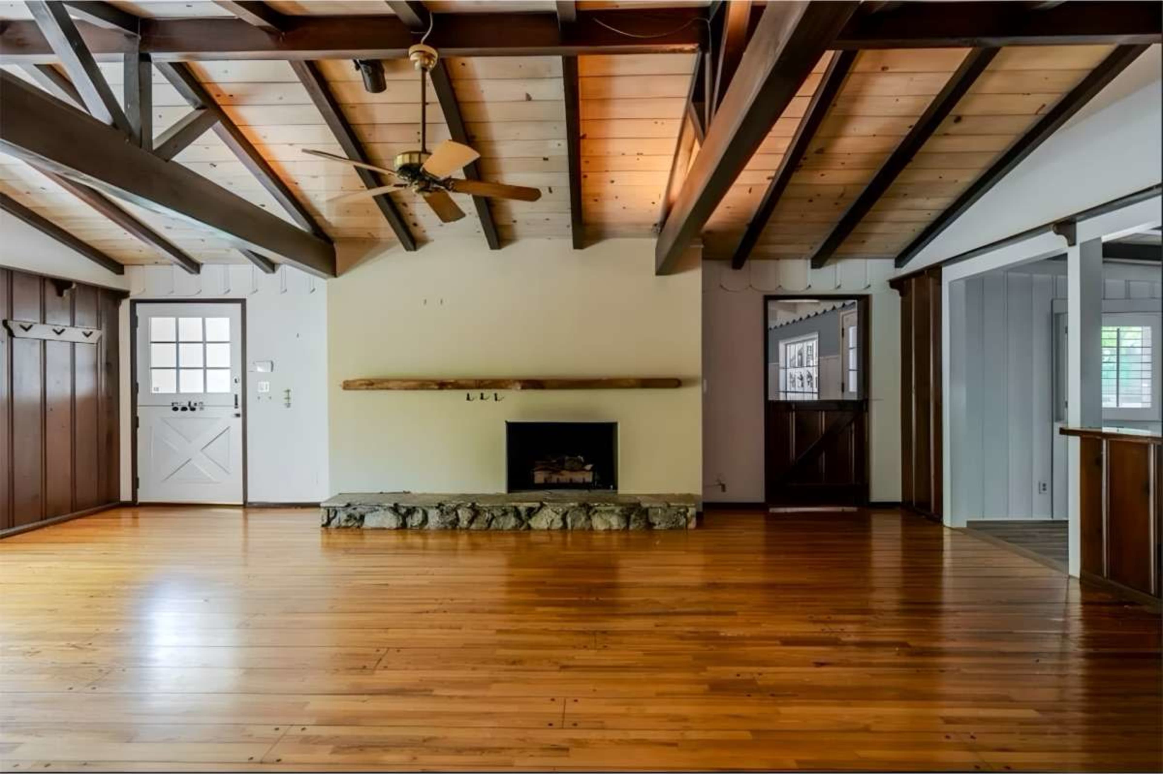 The room features wooden beams, a stone fireplace, and polished hardwood floors, creating an open and spacious layout.
