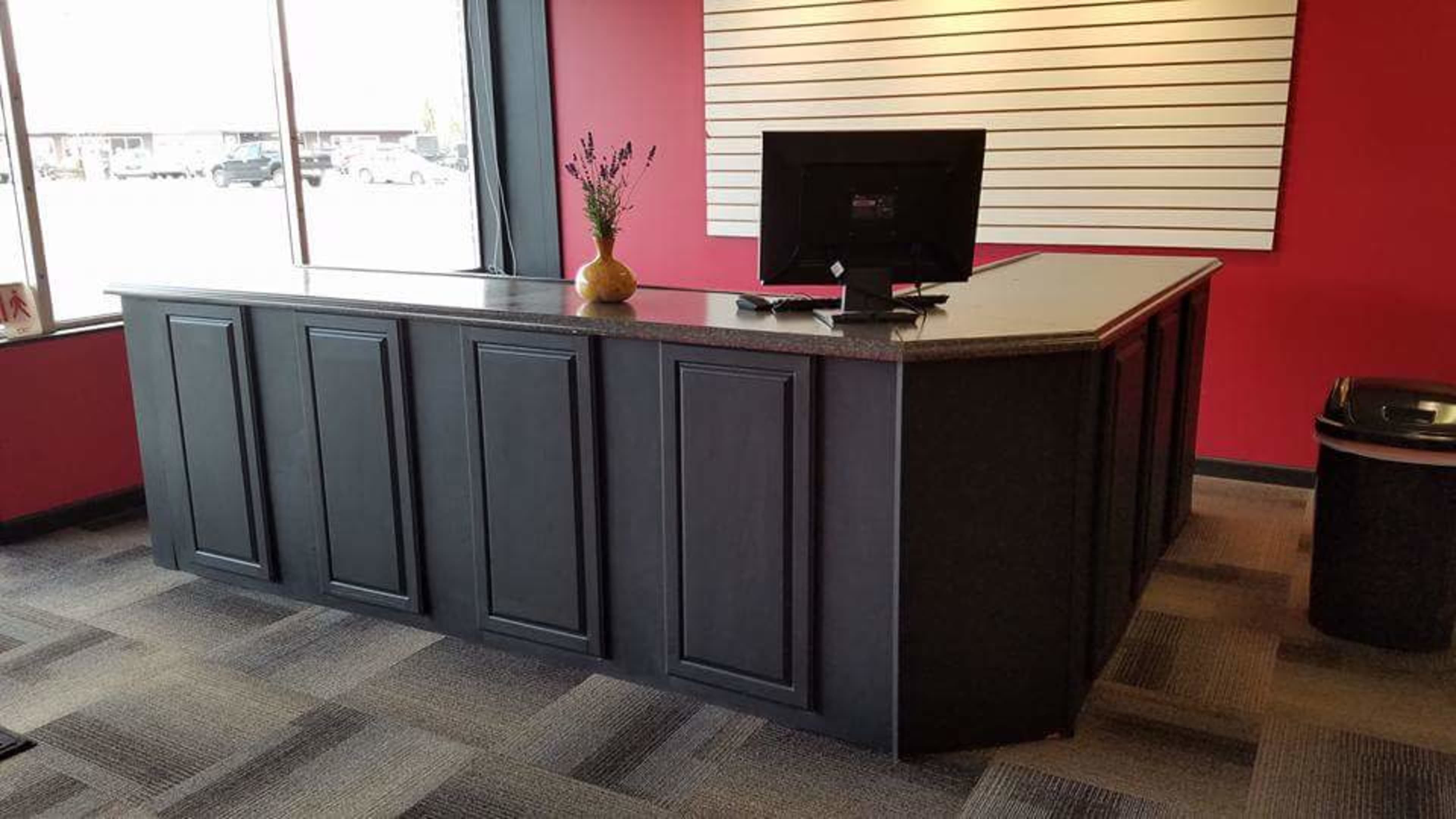A black reception desk with a granite countertop, backed by a red wall and featuring a monitor on top.