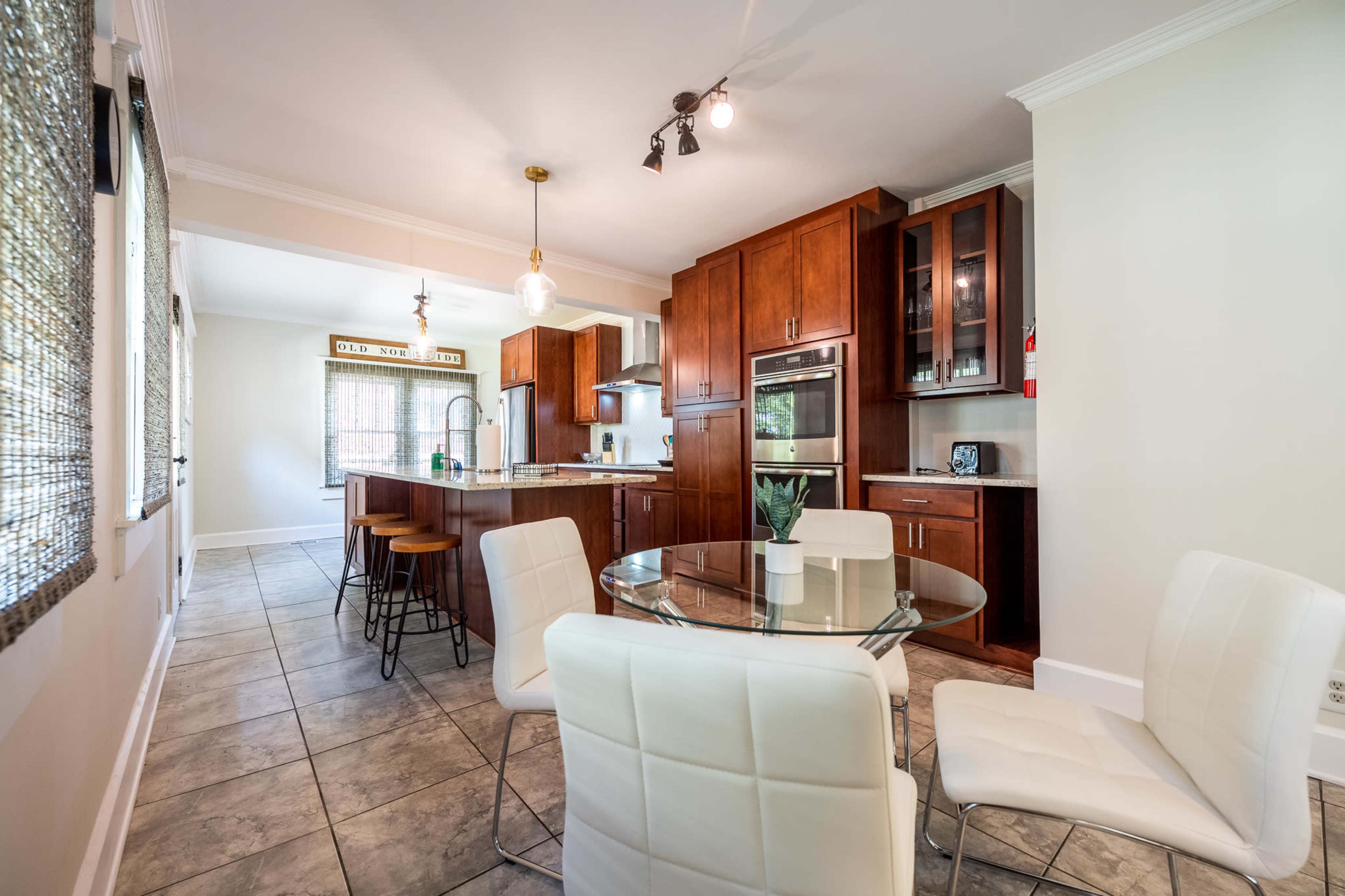 A modern kitchen and dining area with wooden cabinets, a glass dining table, and white chairs.