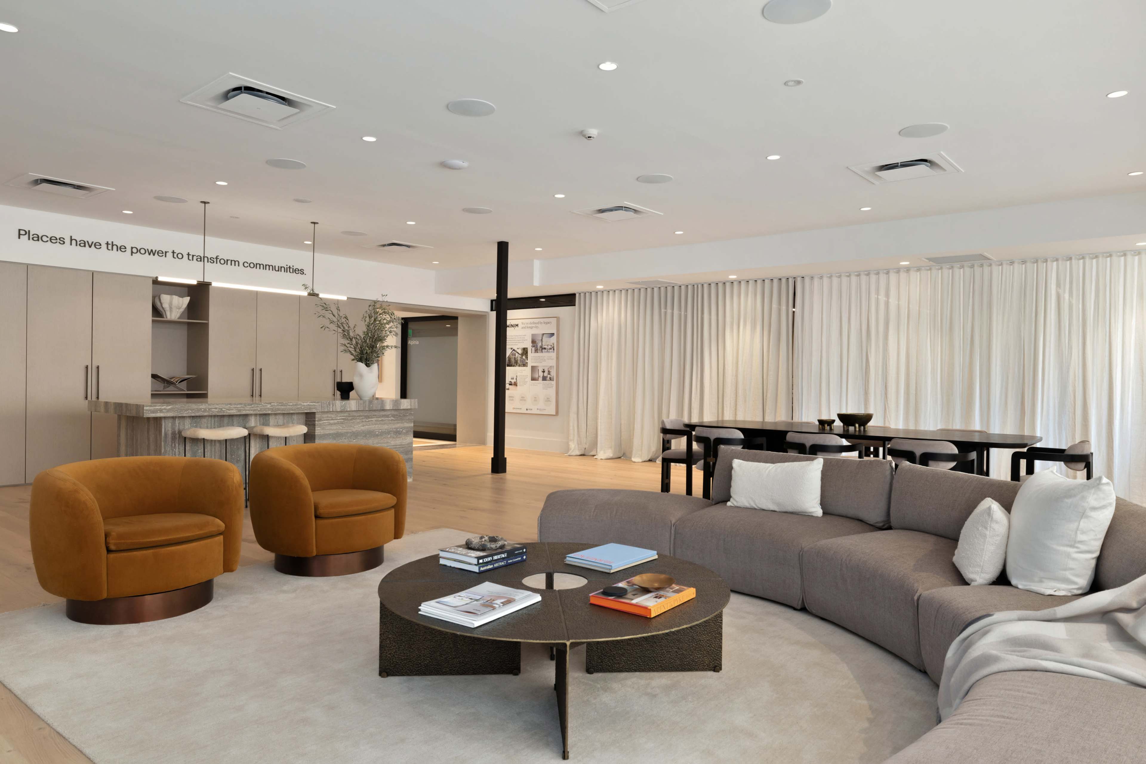 The image shows a modern interior living space featuring a curved sofa, two armchairs, a circular coffee table, and a dining area with a long table and chairs.