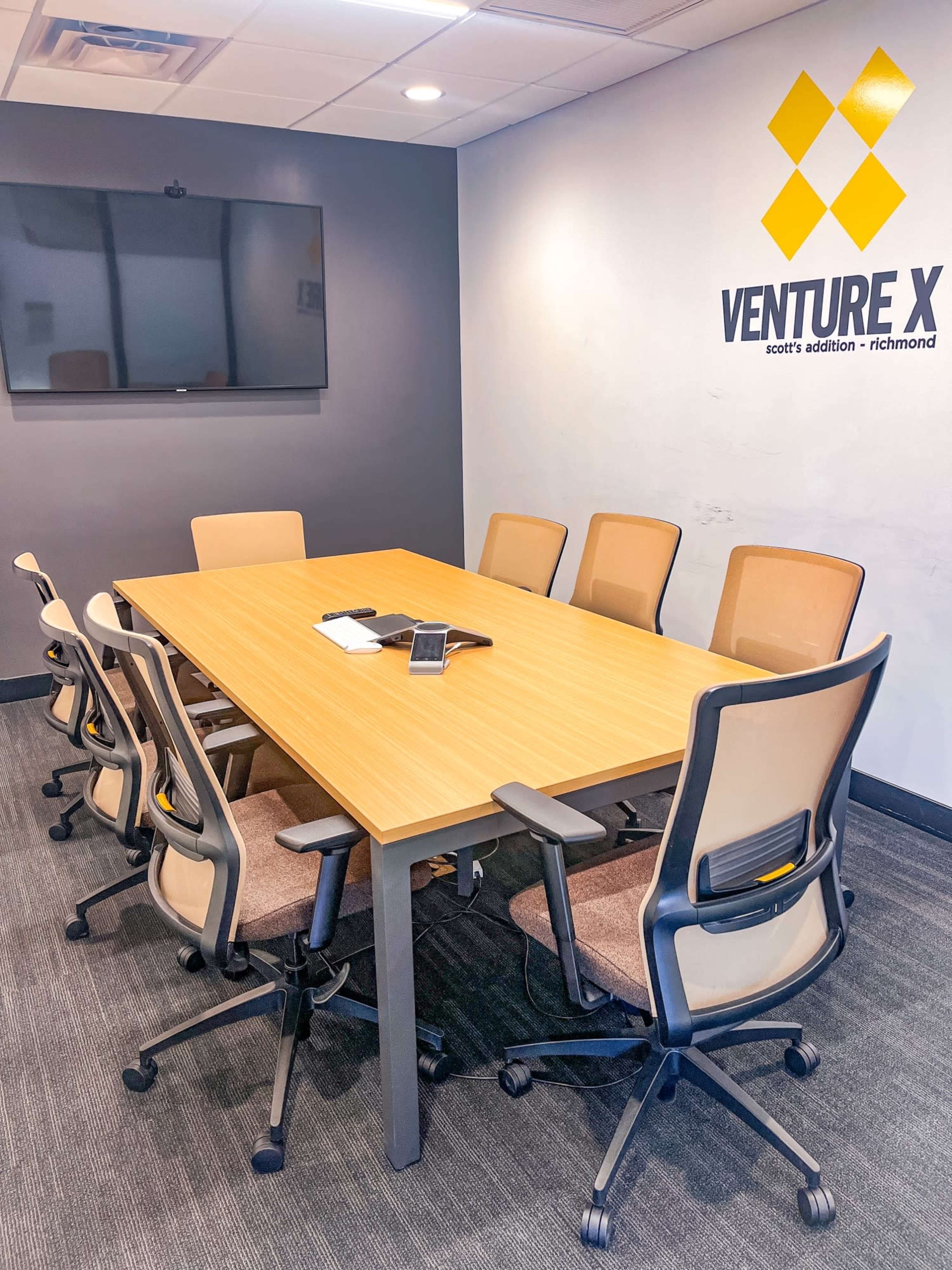 A modern conference room with a large wooden table surrounded by eight ergonomic chairs and a wall-mounted television.