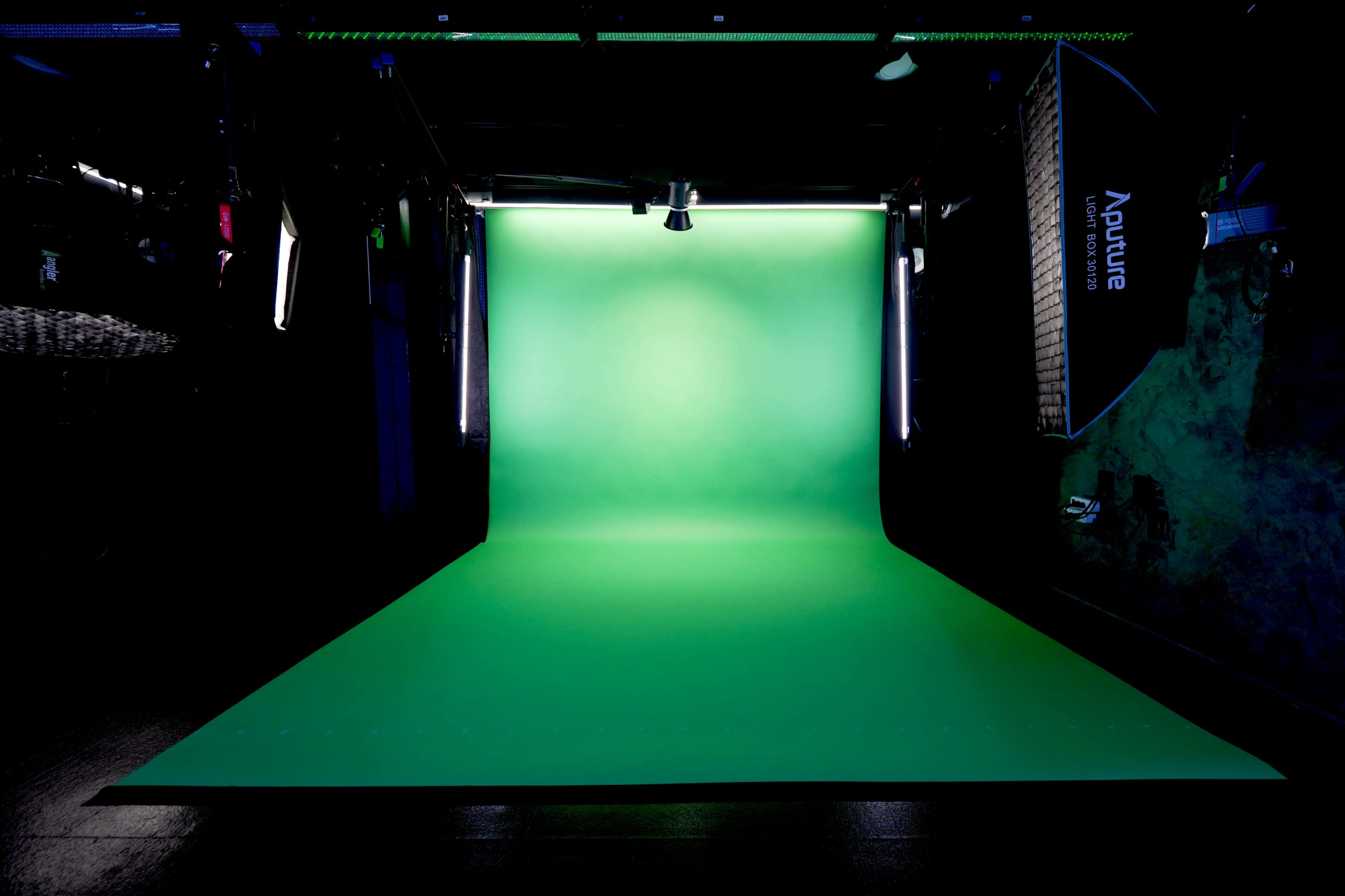 A photography studio with a bright green backdrop and studio lighting equipment set up on either side.