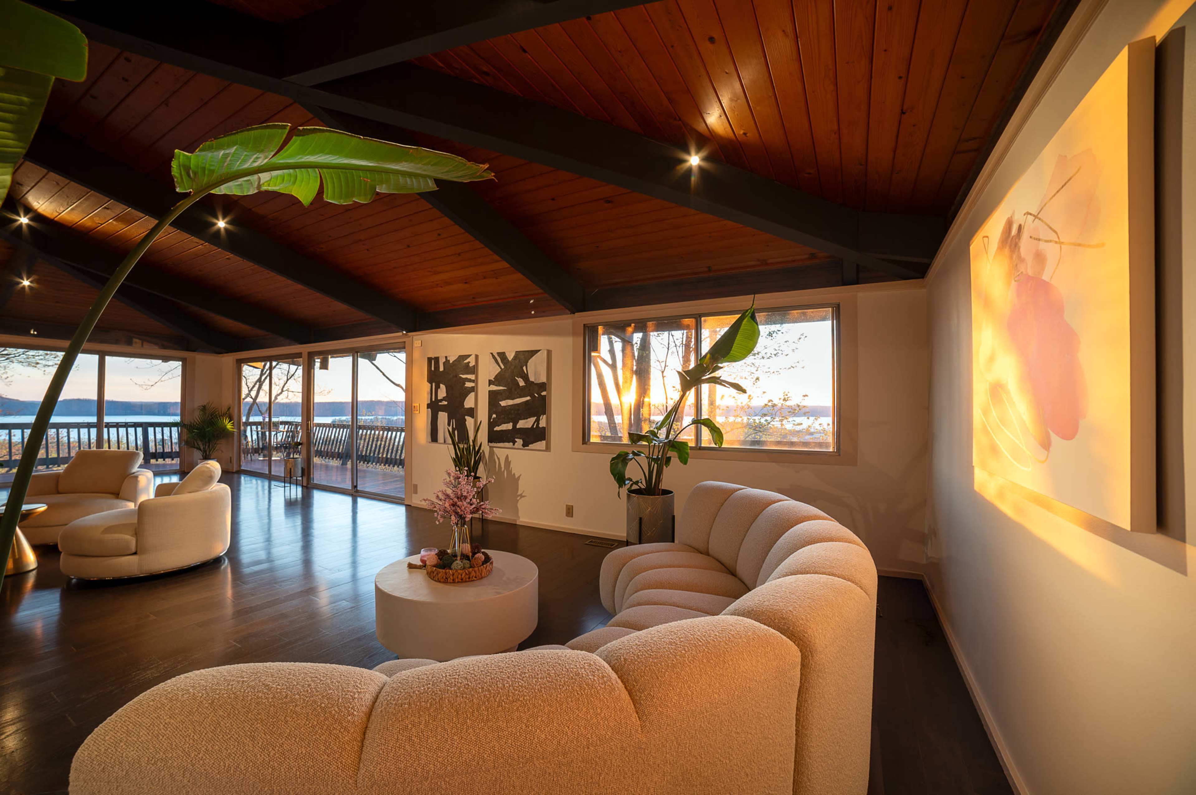 A modern living room features a curved white sofa, a round coffee table, and large windows overlooking a scenic view.