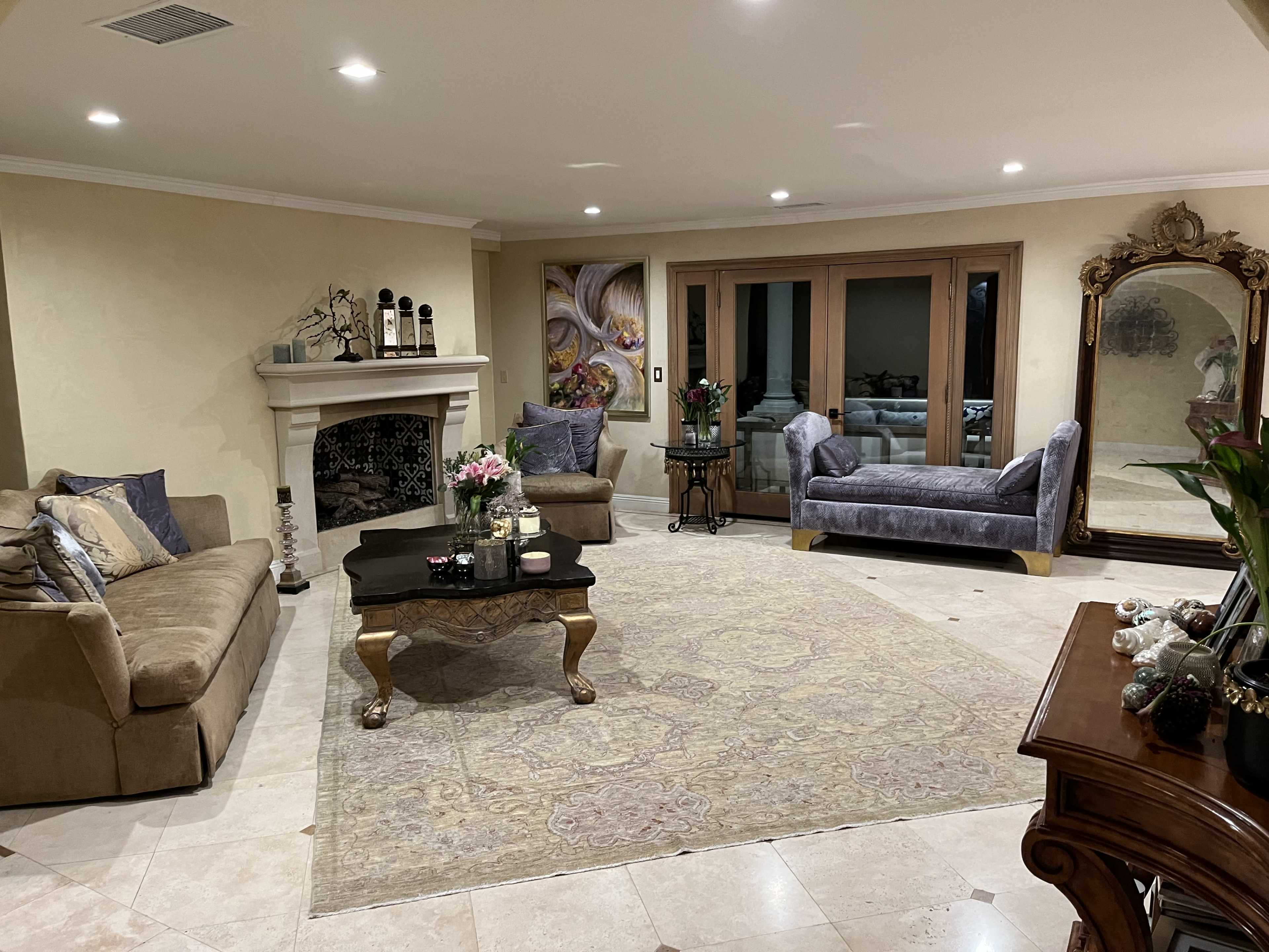 The living room features a beige sofa and a purple armchair facing a glass coffee table, with a fireplace and large mirror visible in the background.