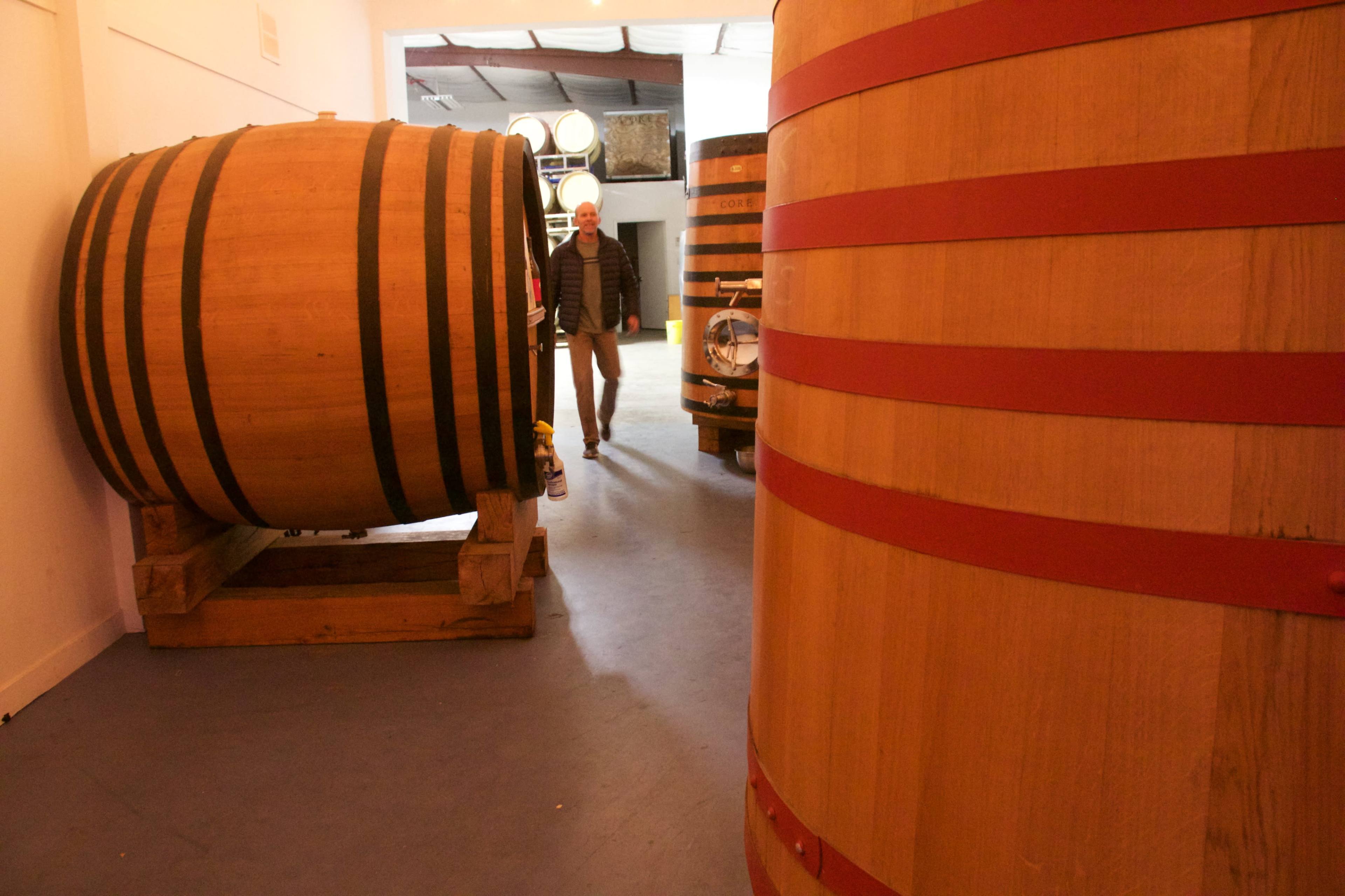 A man walks near two large wooden barrels in a warehouse.