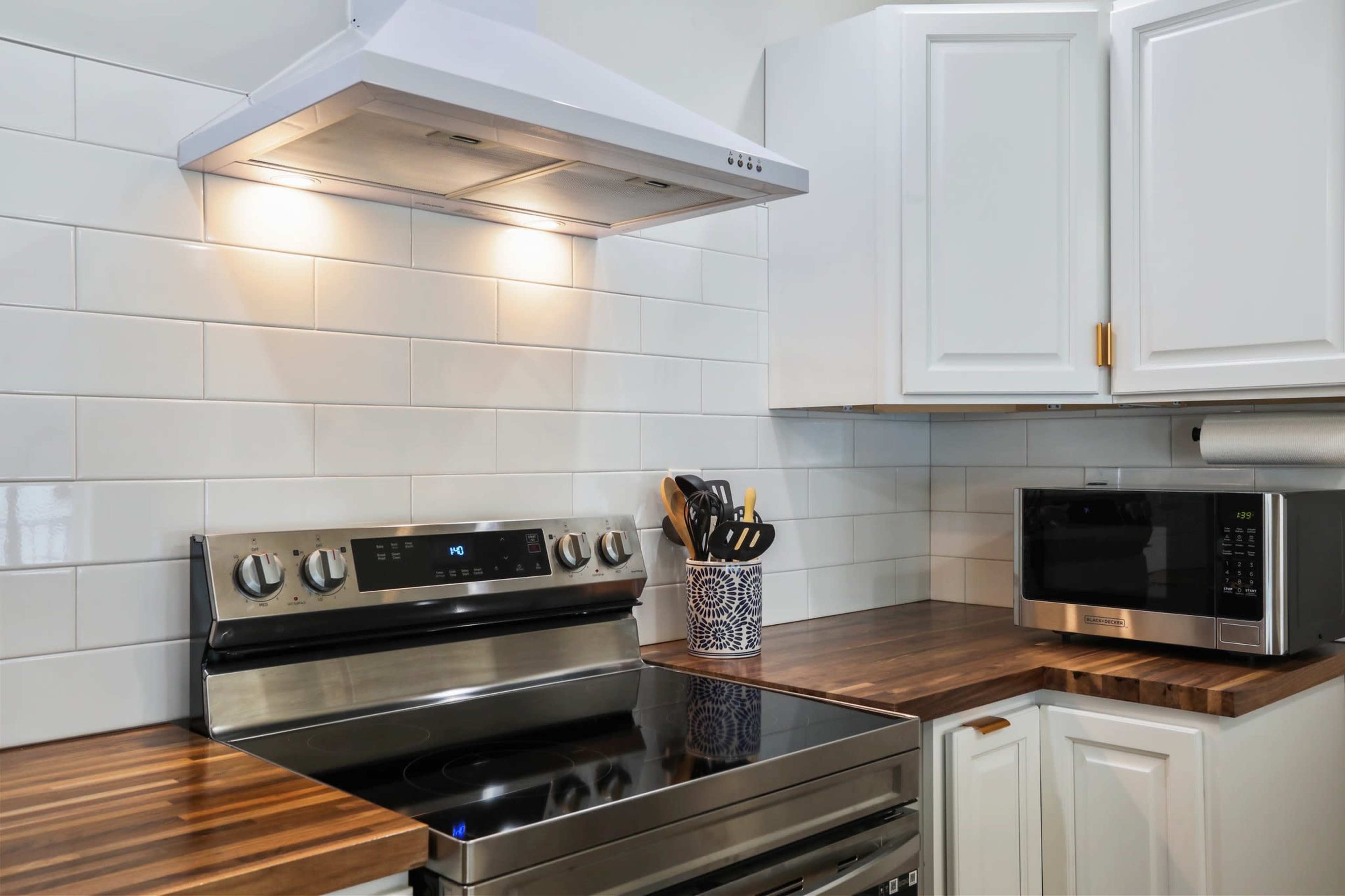 A modern kitchen featuring a stainless steel stove, white cabinets, a microwave, and a wooden countertop.