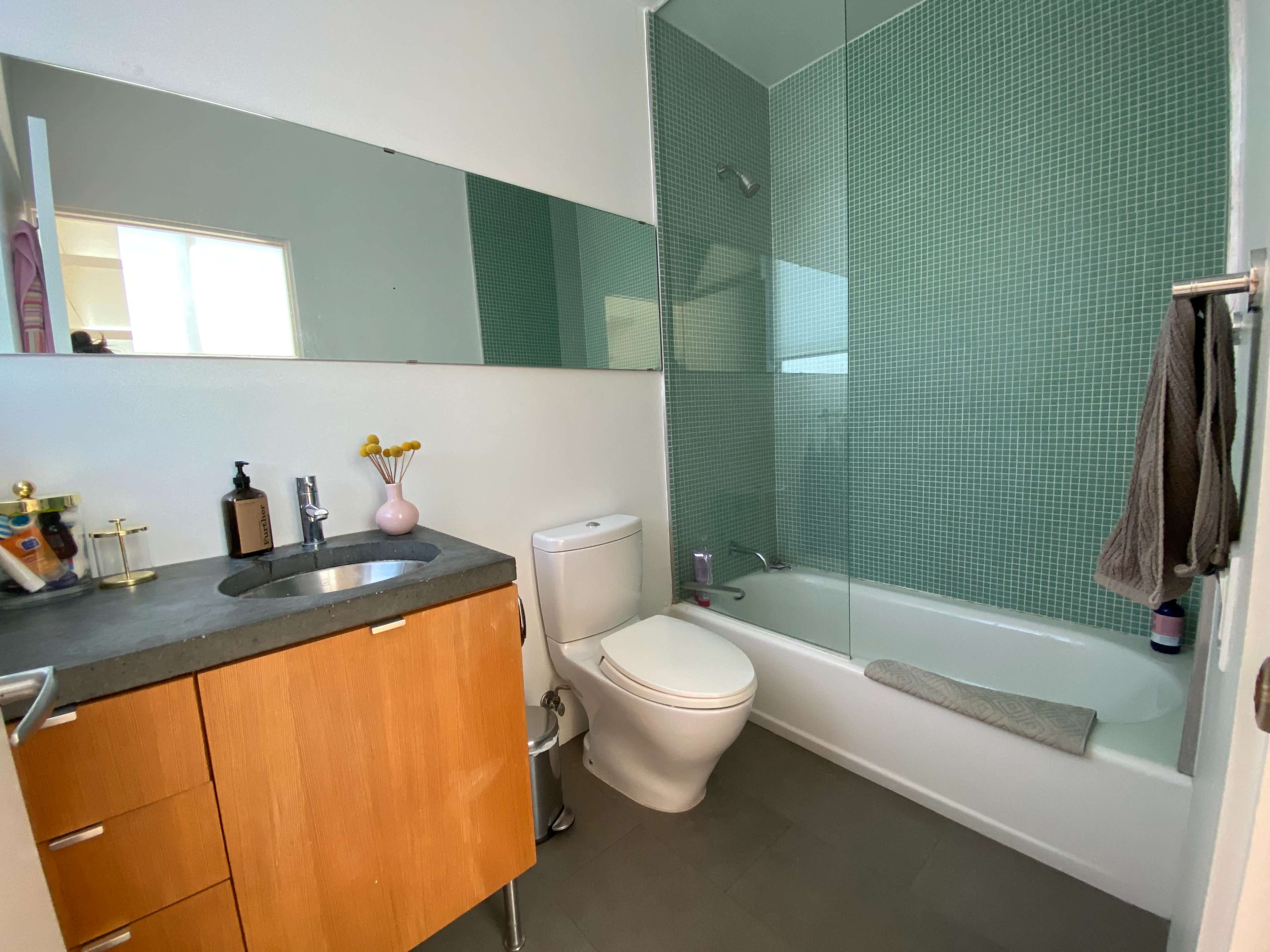 A modern bathroom featuring a bathtub with a glass shower partition, a toilet, and a sink with a wooden cabinet.