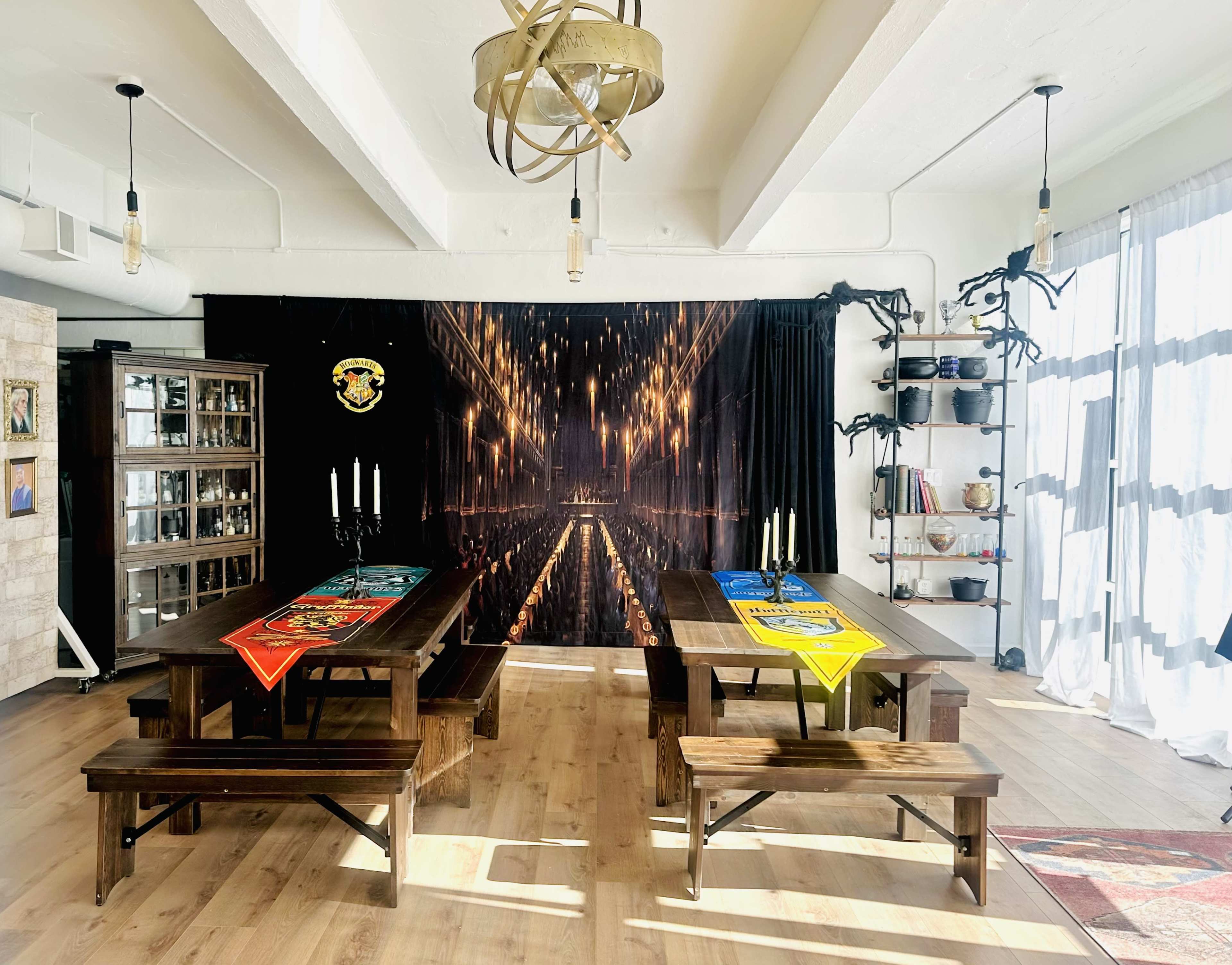 The image shows a dining area with long wooden tables and benches, decorated with house banners and a backdrop featuring a grand hall illuminated by lights.