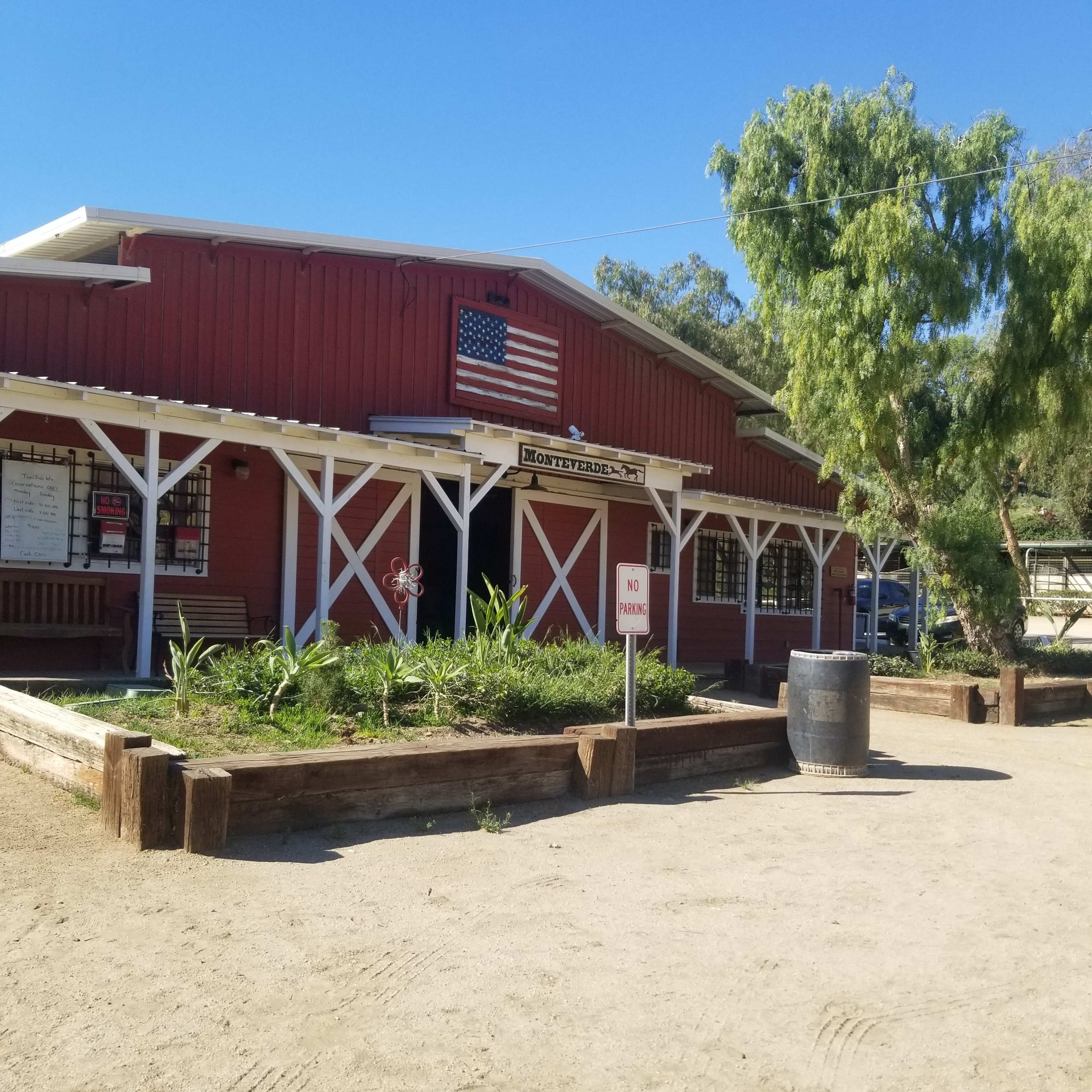 A red barn-like building with an American flag on the facade, surrounded by a garden and a dirt pathway.
