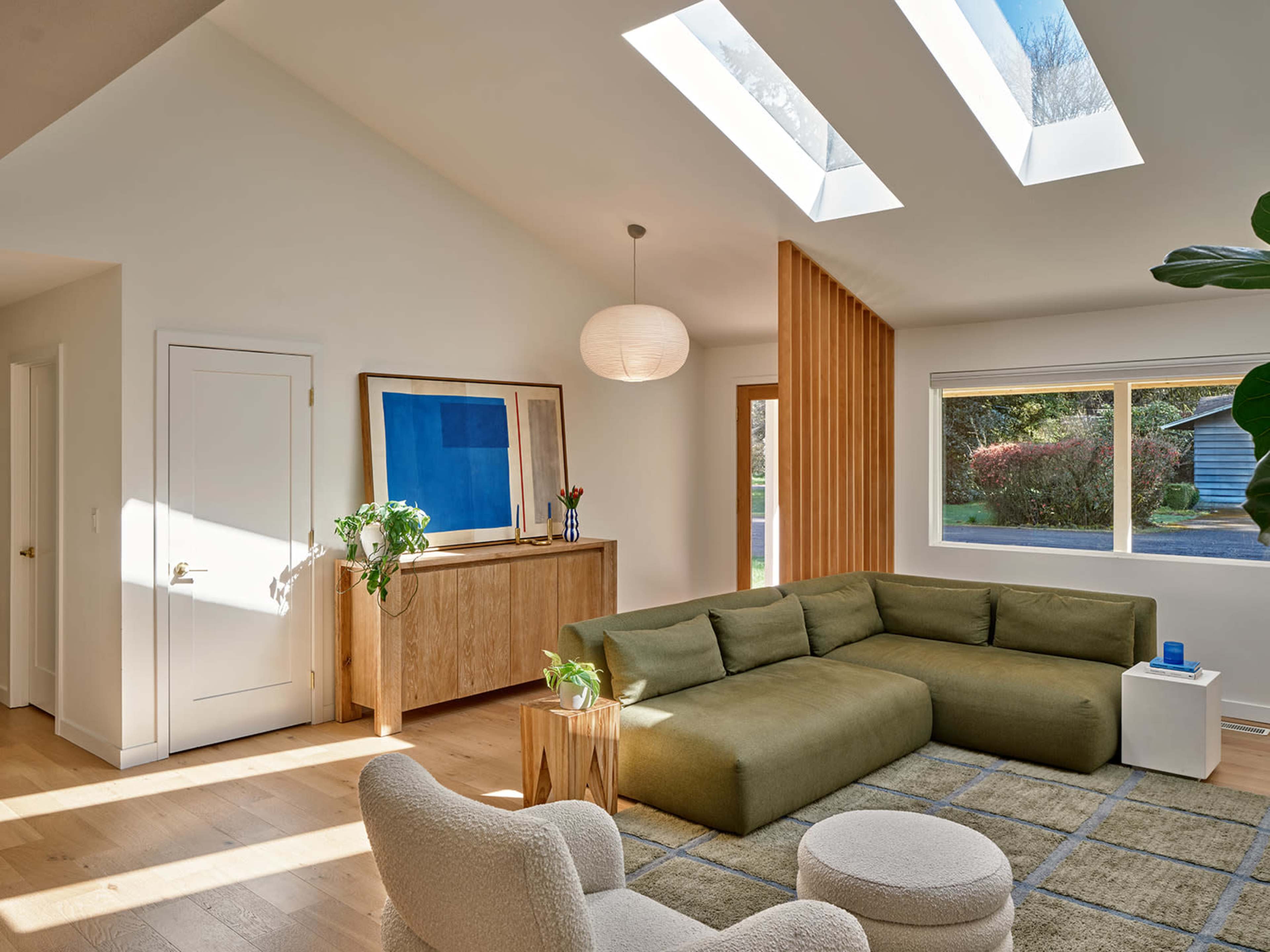 The image shows a modern living room with a green sectional sofa, a wooden sideboard, and large skylights letting in natural light.
