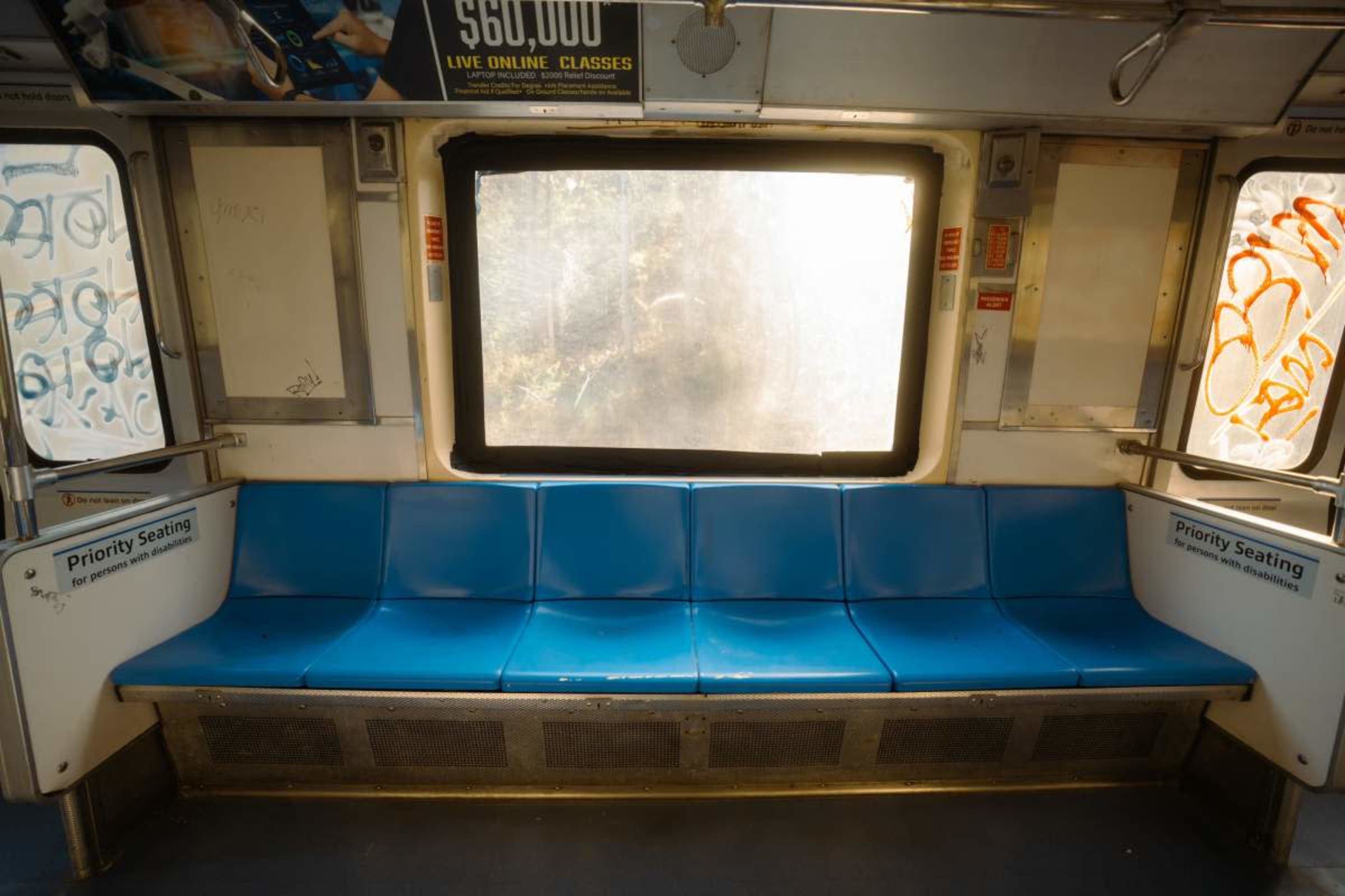 An empty subway car features blue benches and a large, foggy window.
