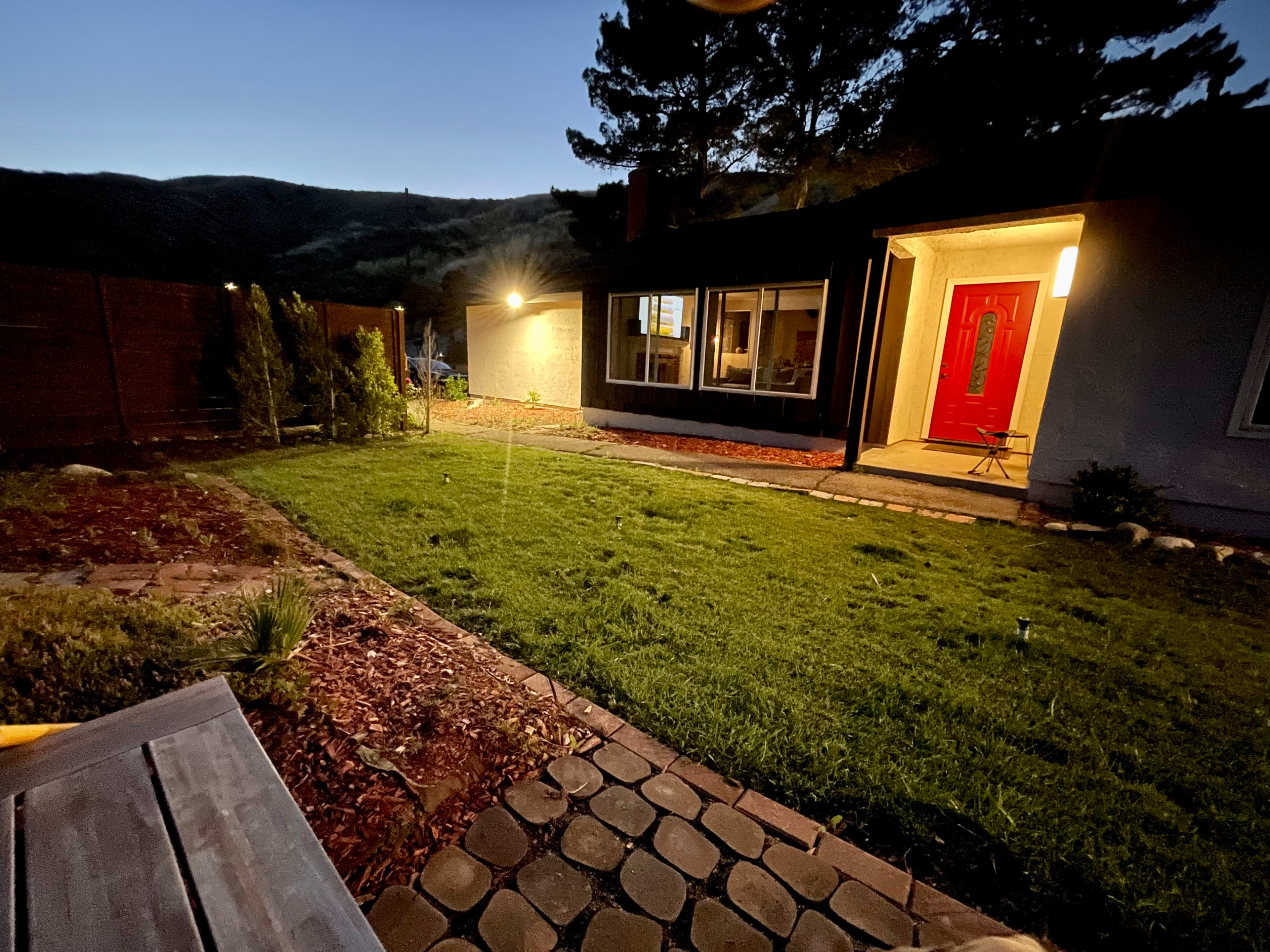 A well-maintained backyard features a lawn and stone pathway, illuminated by a porch light under a twilight sky.
