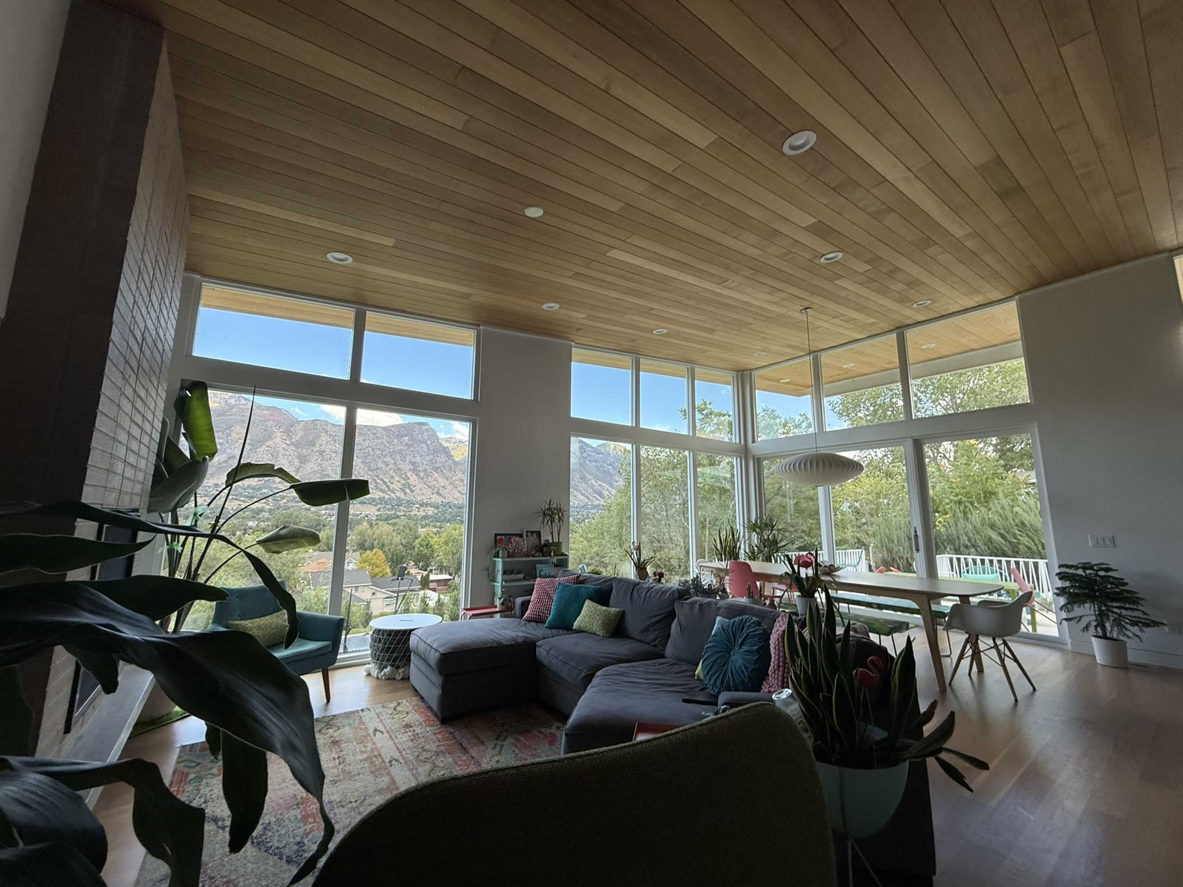 A modern living room features large windows showcasing mountain views, a comfortable sectional sofa, and various indoor plants.