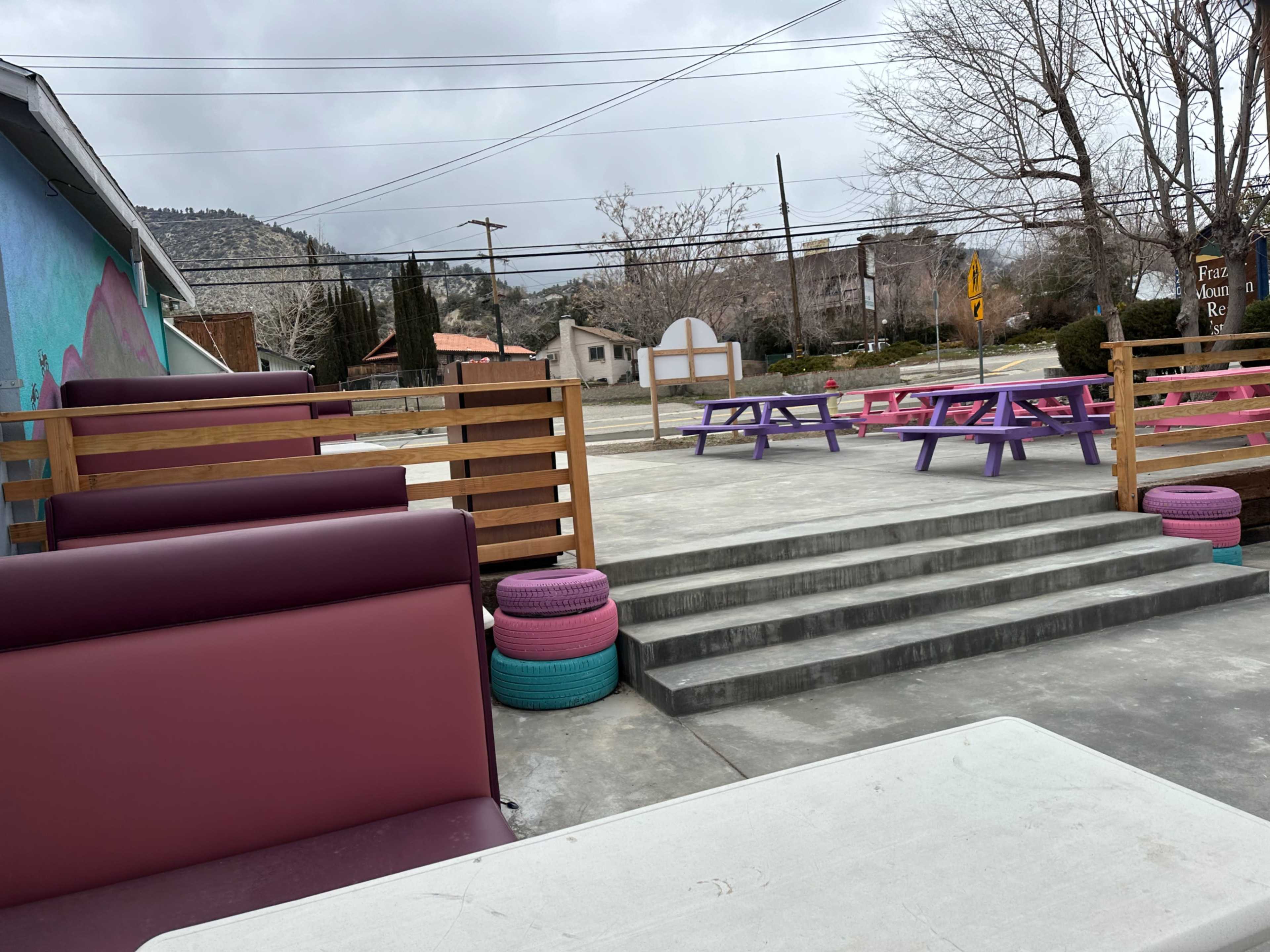 An outdoor seating area with colorful benches and tables, surrounded by a gray sky and sparse trees.