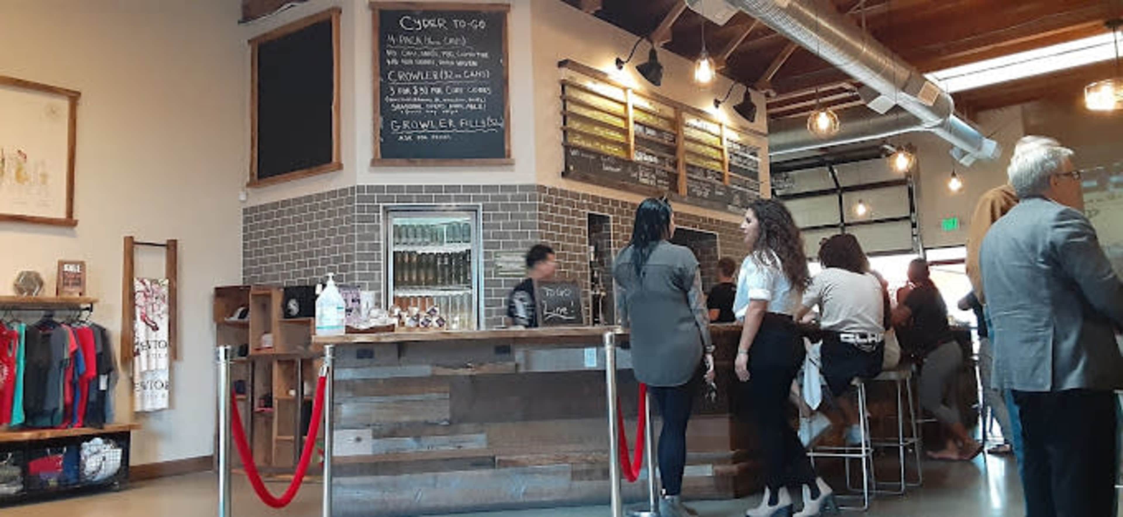 The image shows a busy café with a service counter at the front and customers seated at high tables.
