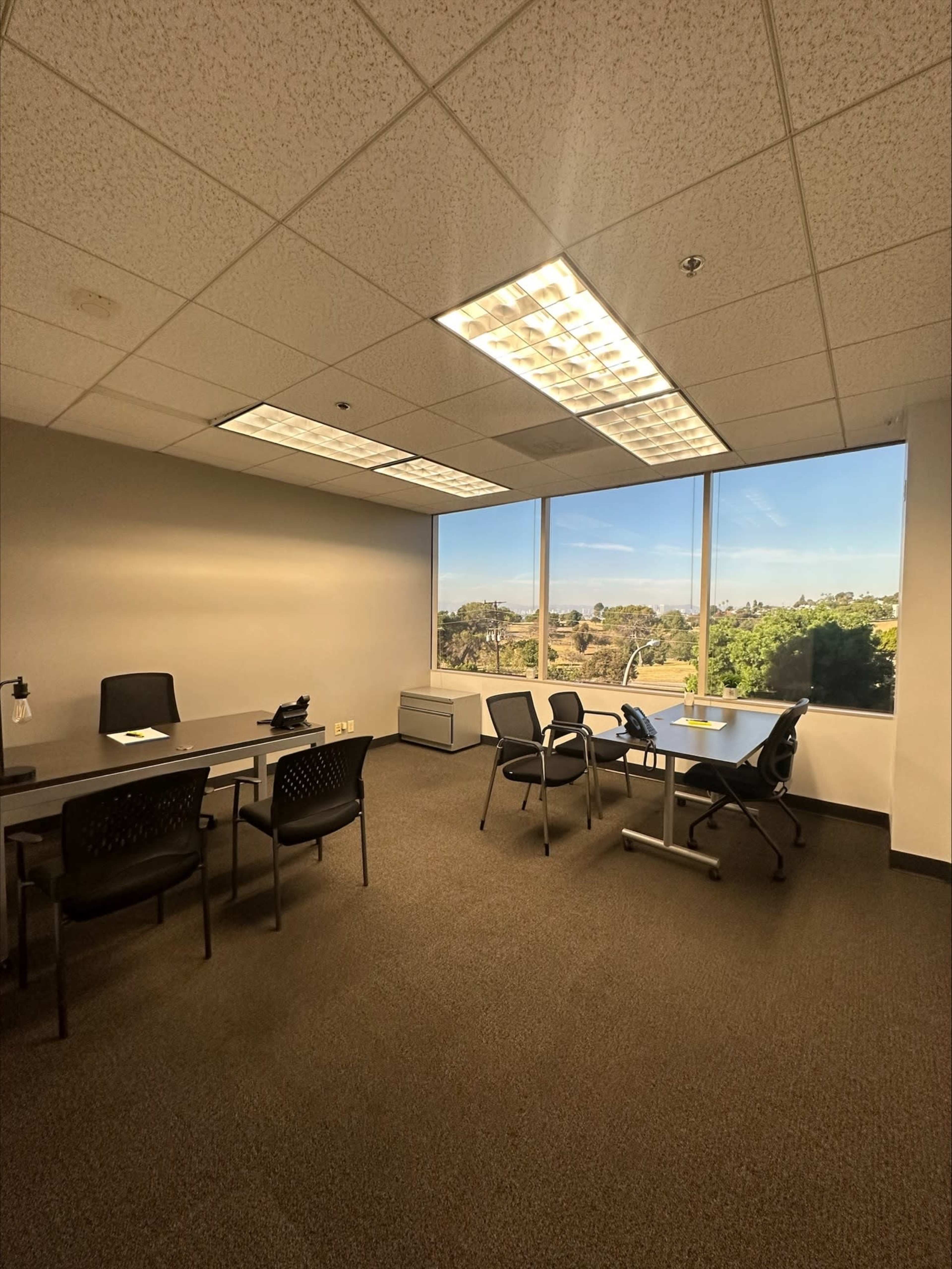 An empty office space features a large window with a view and several chairs arranged around a table.