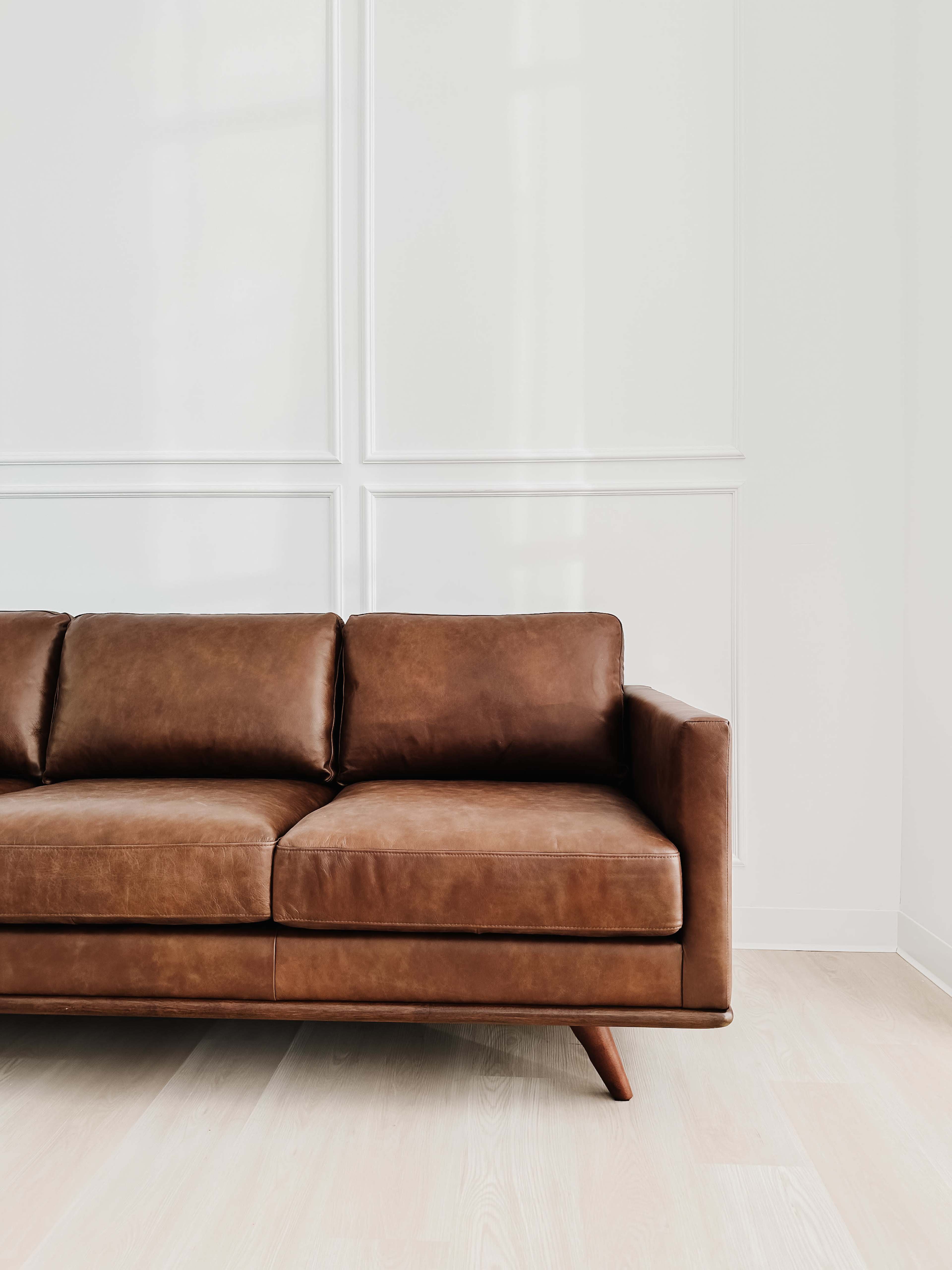 A brown leather sofa is positioned against a light-colored wall in a minimalist room.