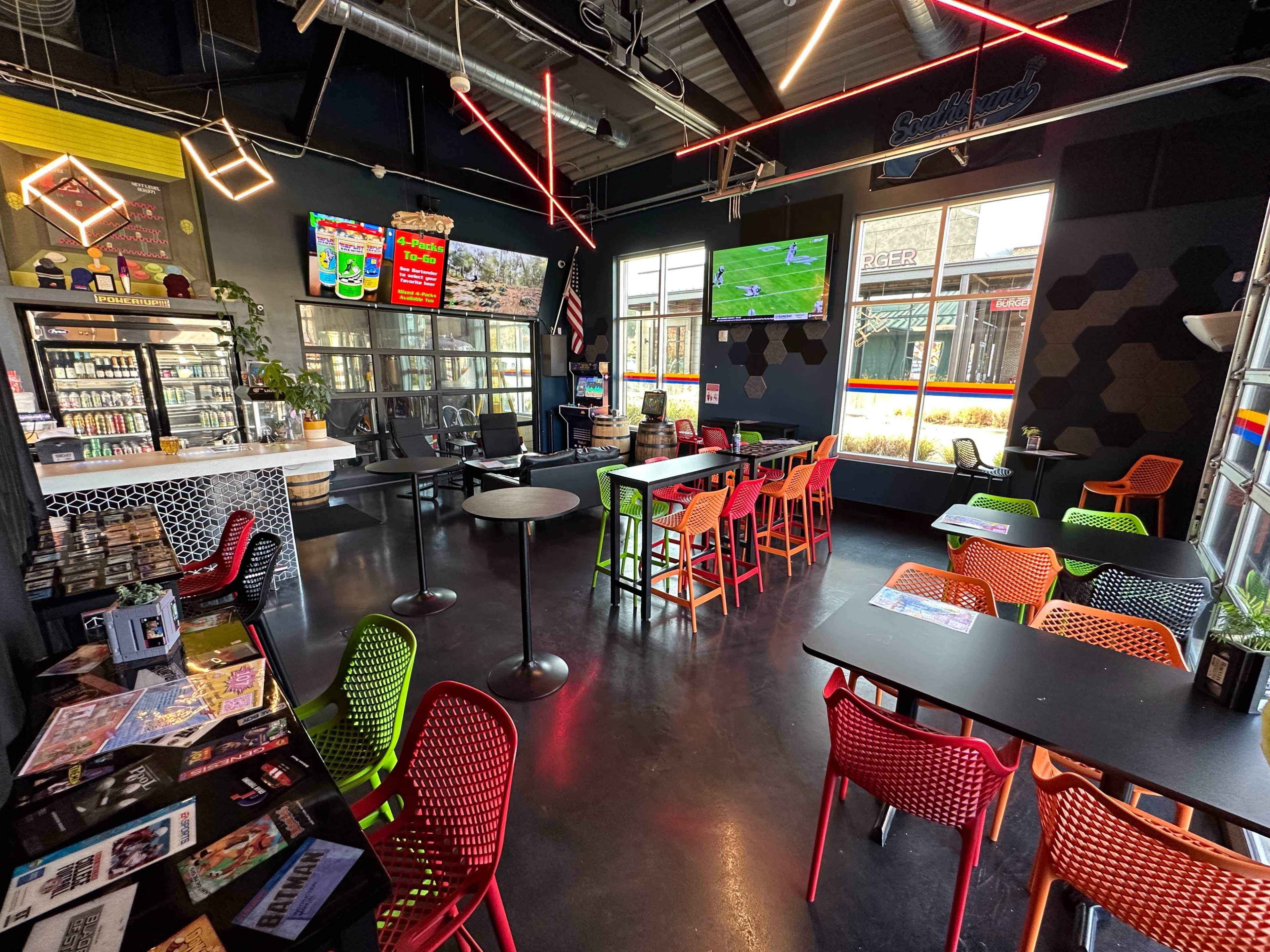 The interior of a modern café features colorful seating, a counter displaying snacks, and a TV broadcasting a sporting event.
