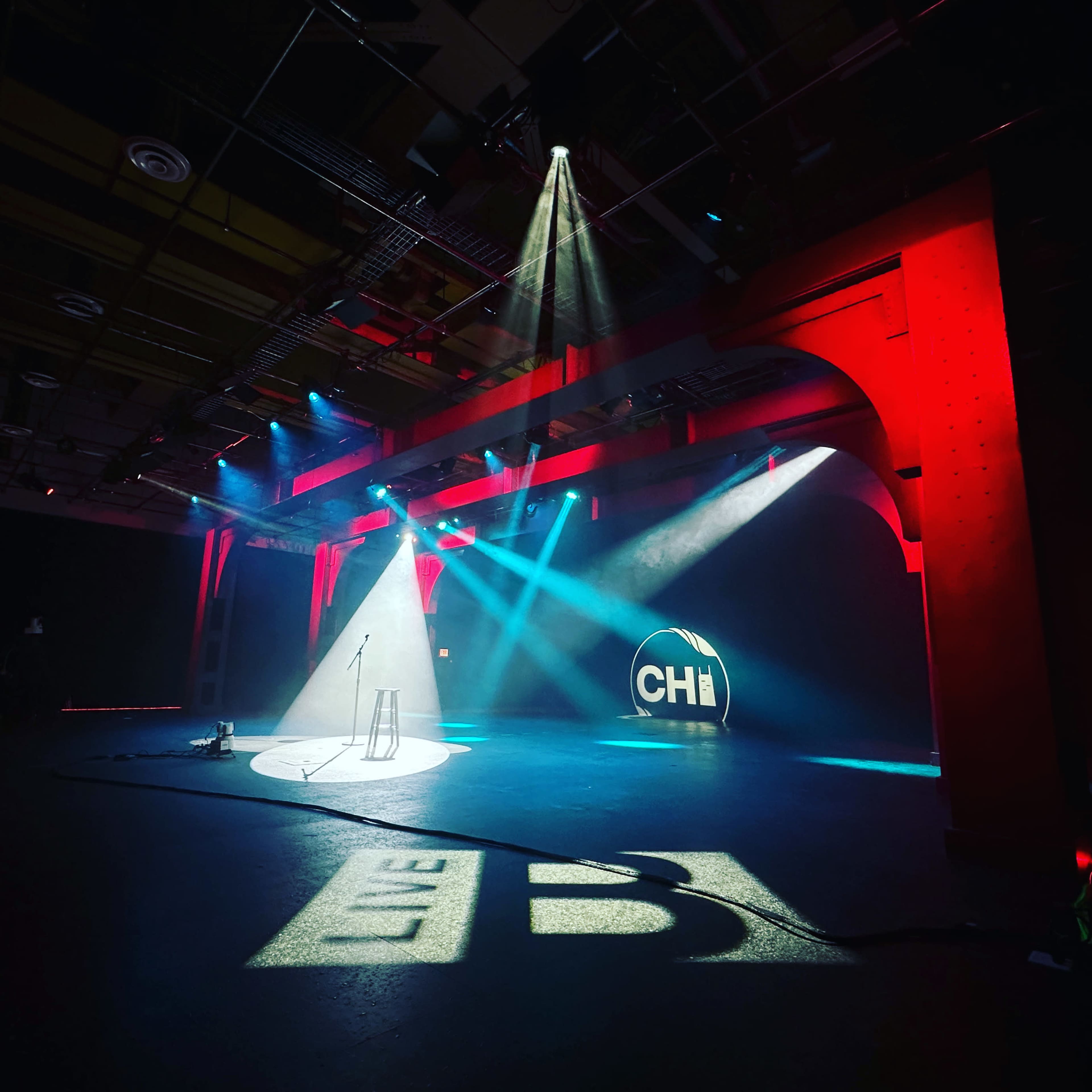 The image shows a performance stage with a microphone stand and illuminated beams of light casting shadows on the floor.