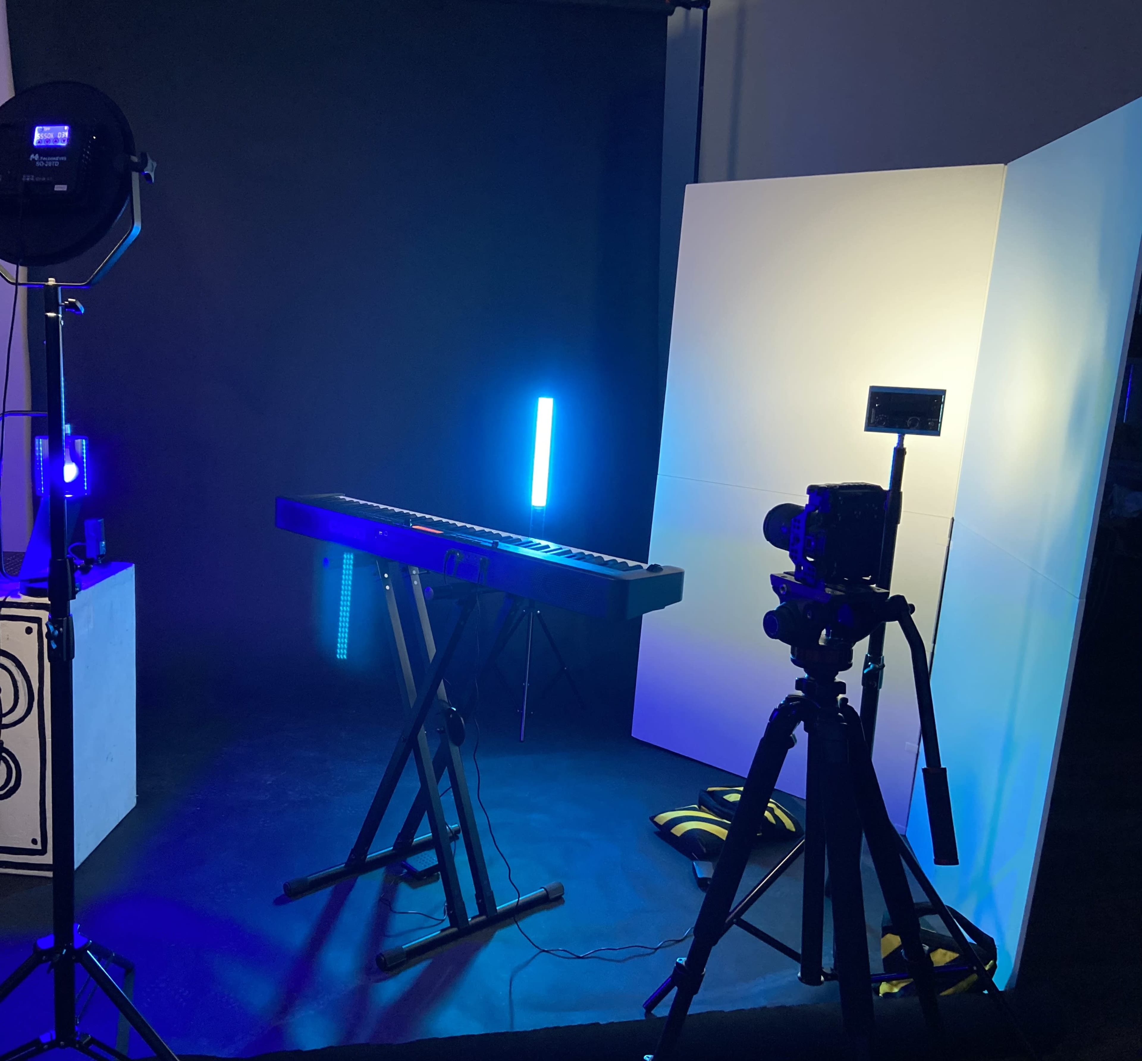 The image shows a music keyboard setup with a camera on a tripod and various lighting elements in a studio environment.