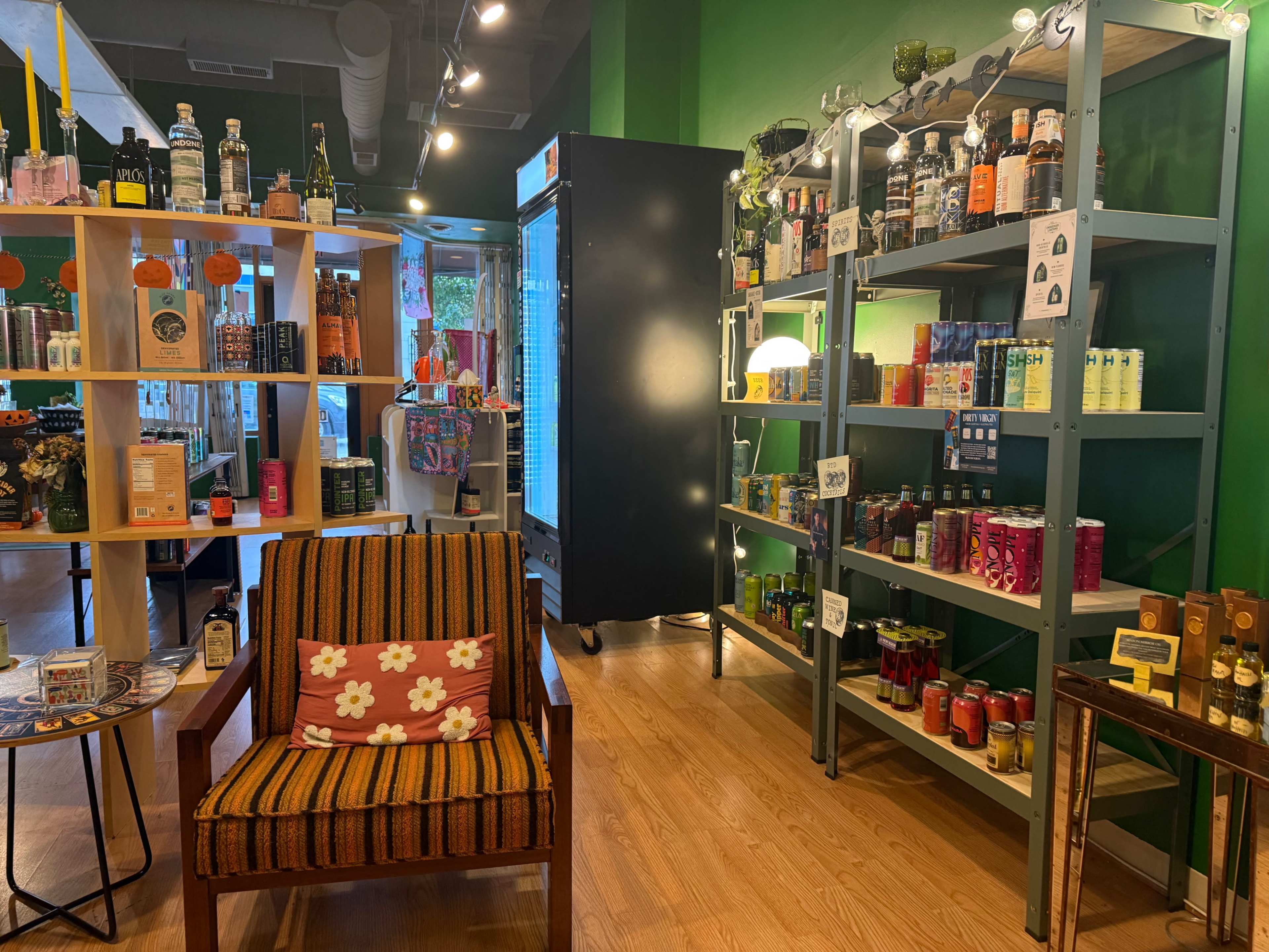 The image shows a boutique interior with shelves displaying various beverages and products, a black fridge, and a patterned chair in the foreground.