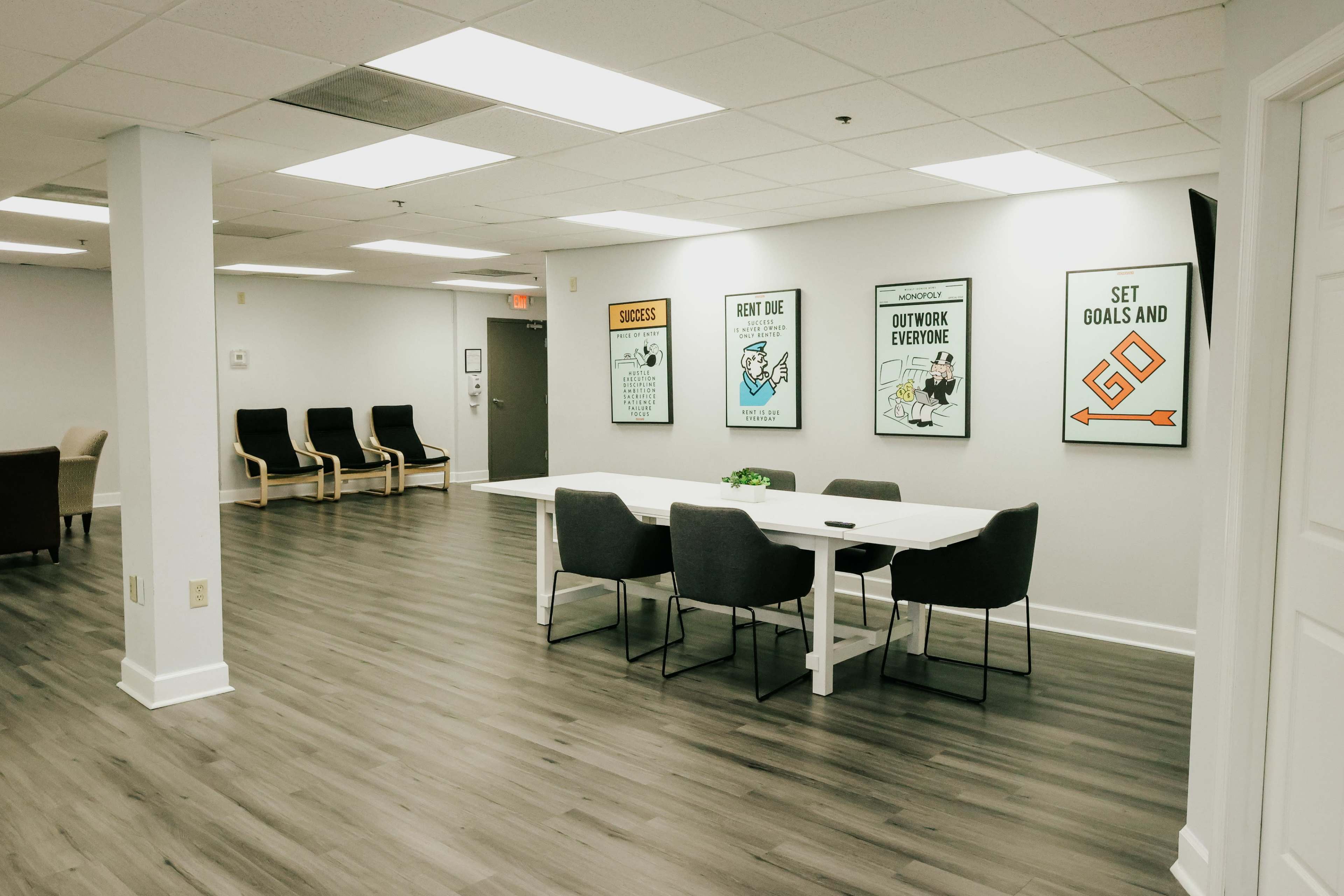 A modern office space featuring a large table with chairs, hardwood flooring, and motivational posters on the walls.