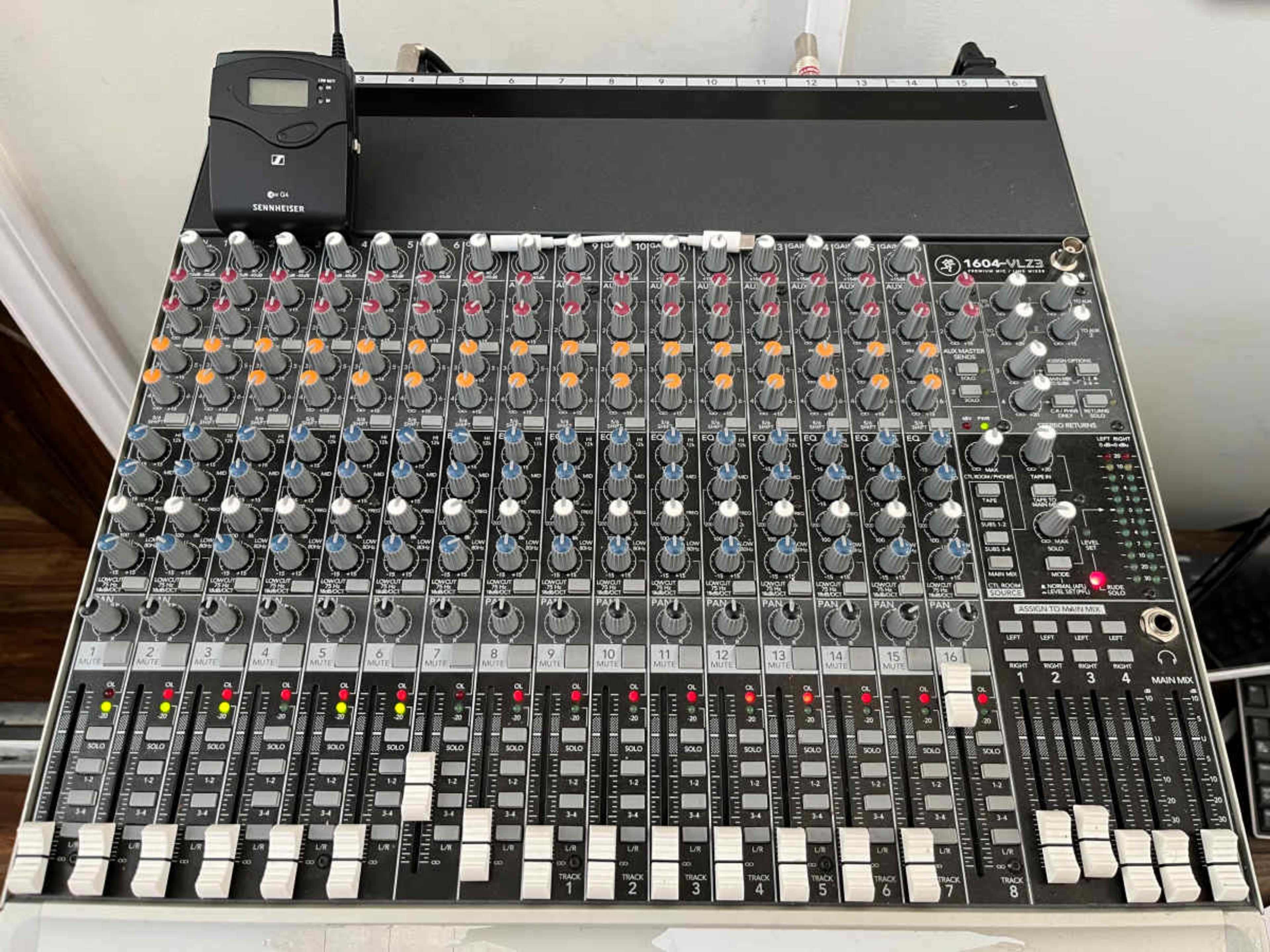 The image shows a professional audio mixing console with various knobs, faders, and input/output connections.