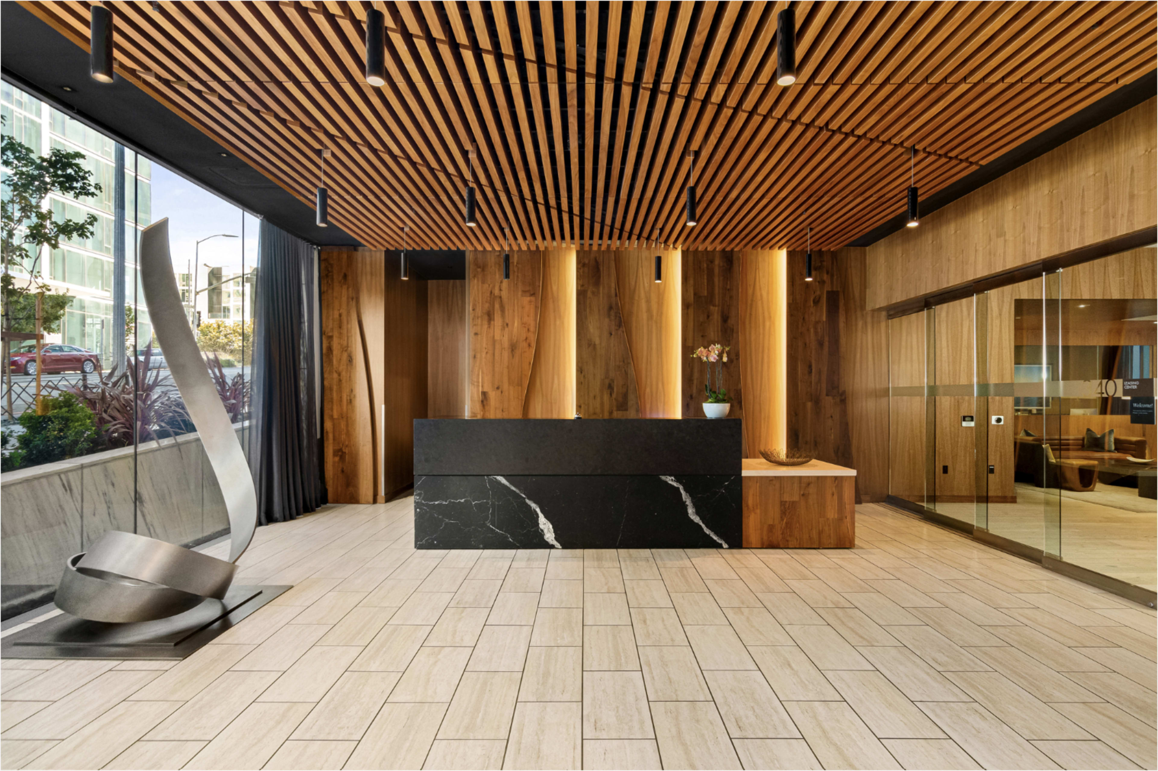 The image shows a modern reception area featuring a sleek black front desk, wooden accents, and a large sculptural piece beside it.