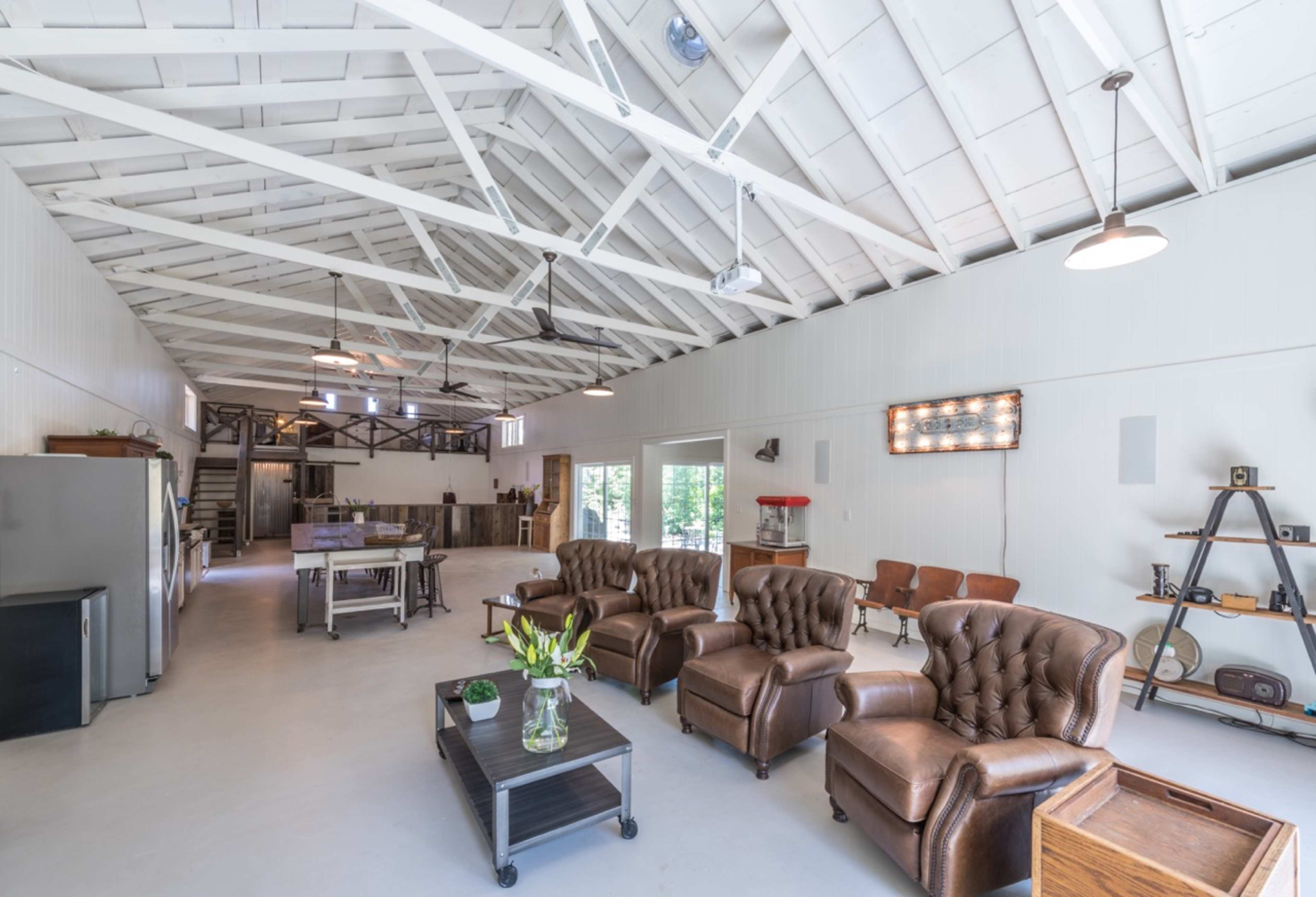 A spacious room with high ceilings, featuring brown leather sofas, a coffee table, a dining area, and industrial-style decor.