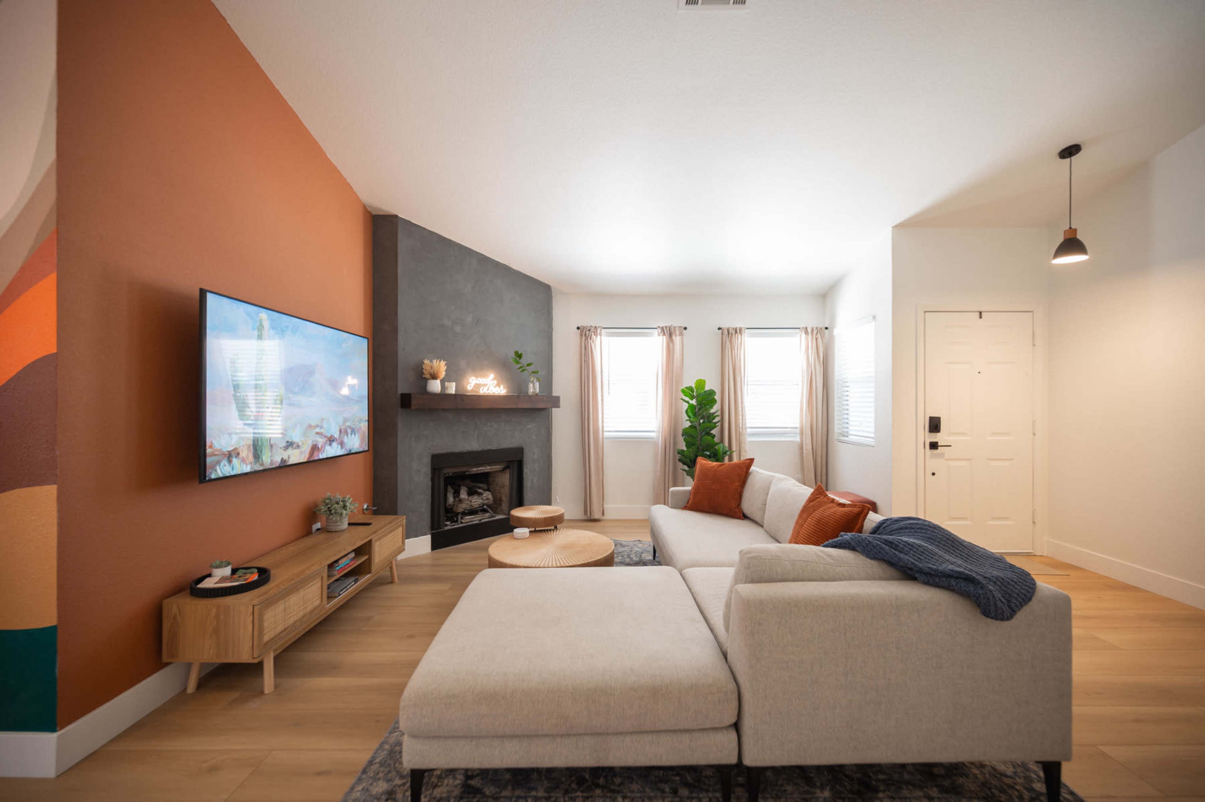 The image shows a modern living room with a sectional sofa, a wooden media console, a fireplace, and a television mounted on the wall.