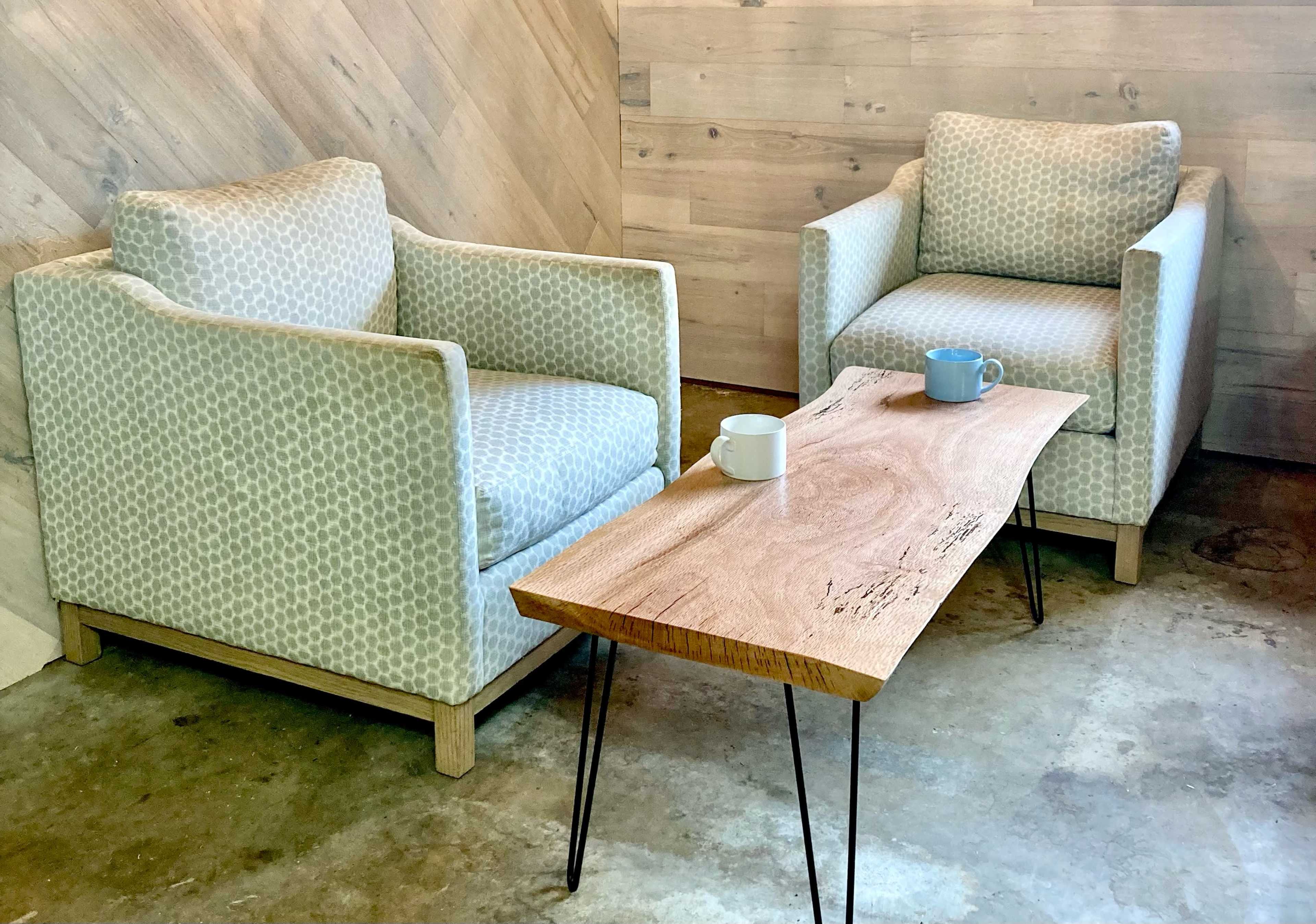 Two upholstered armchairs with geometric patterns are positioned around a wooden coffee table with metal legs in a room with a wood-paneled wall.