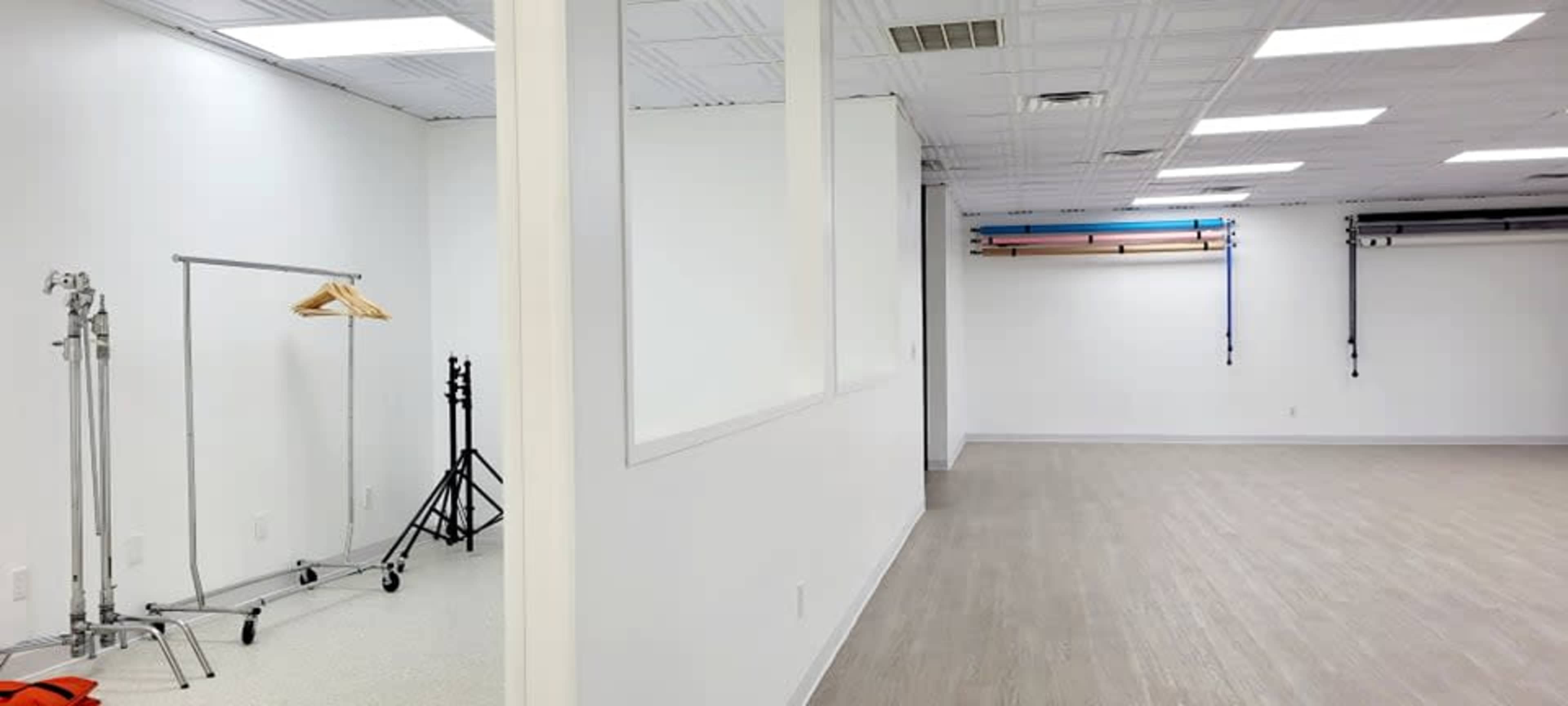A spacious, well-lit room with a clothing rack, photography stands, and backdrops mounted on the wall.