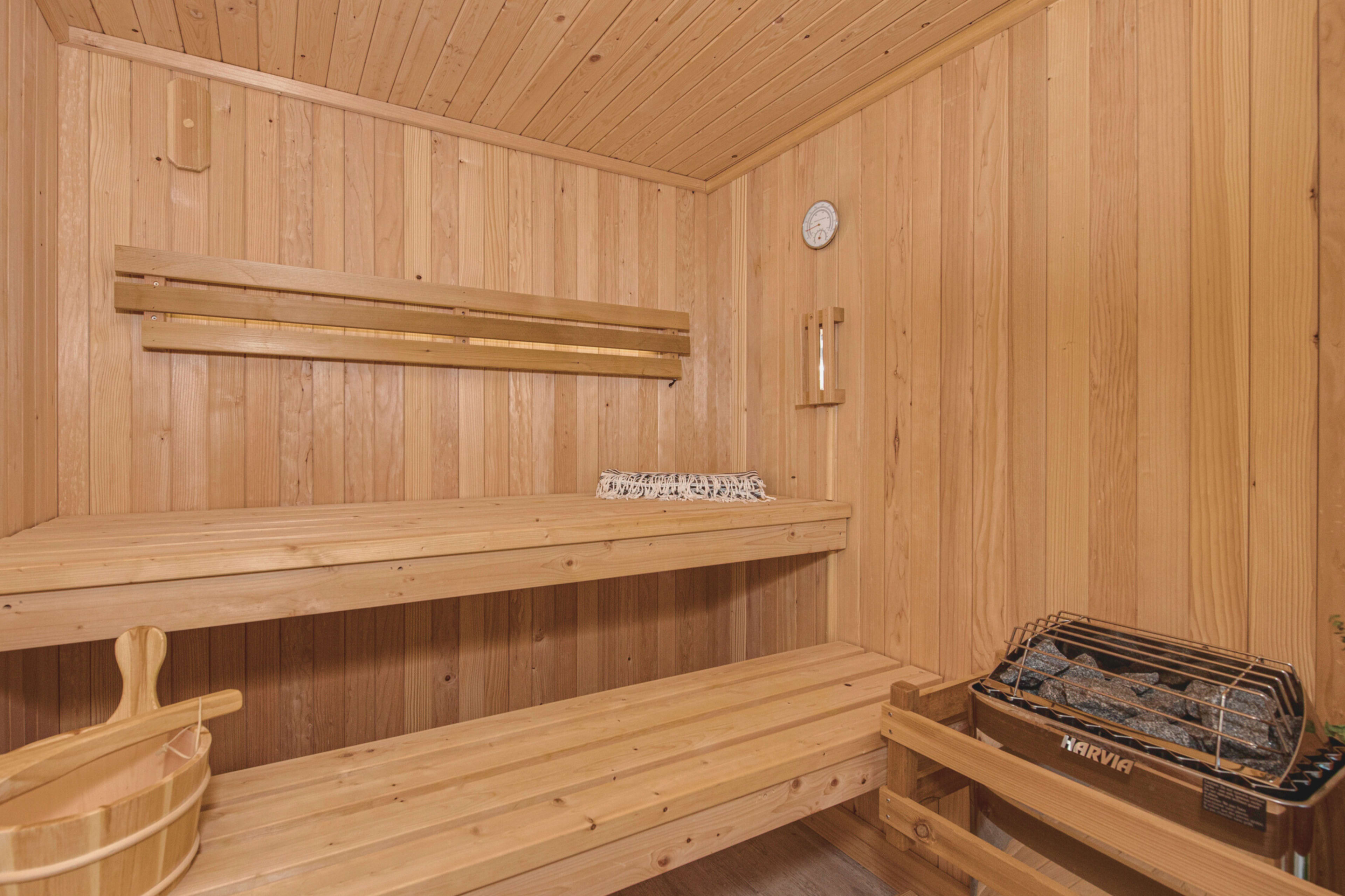 A wooden sauna room with benches, a clock on the wall, and a heater on the floor.