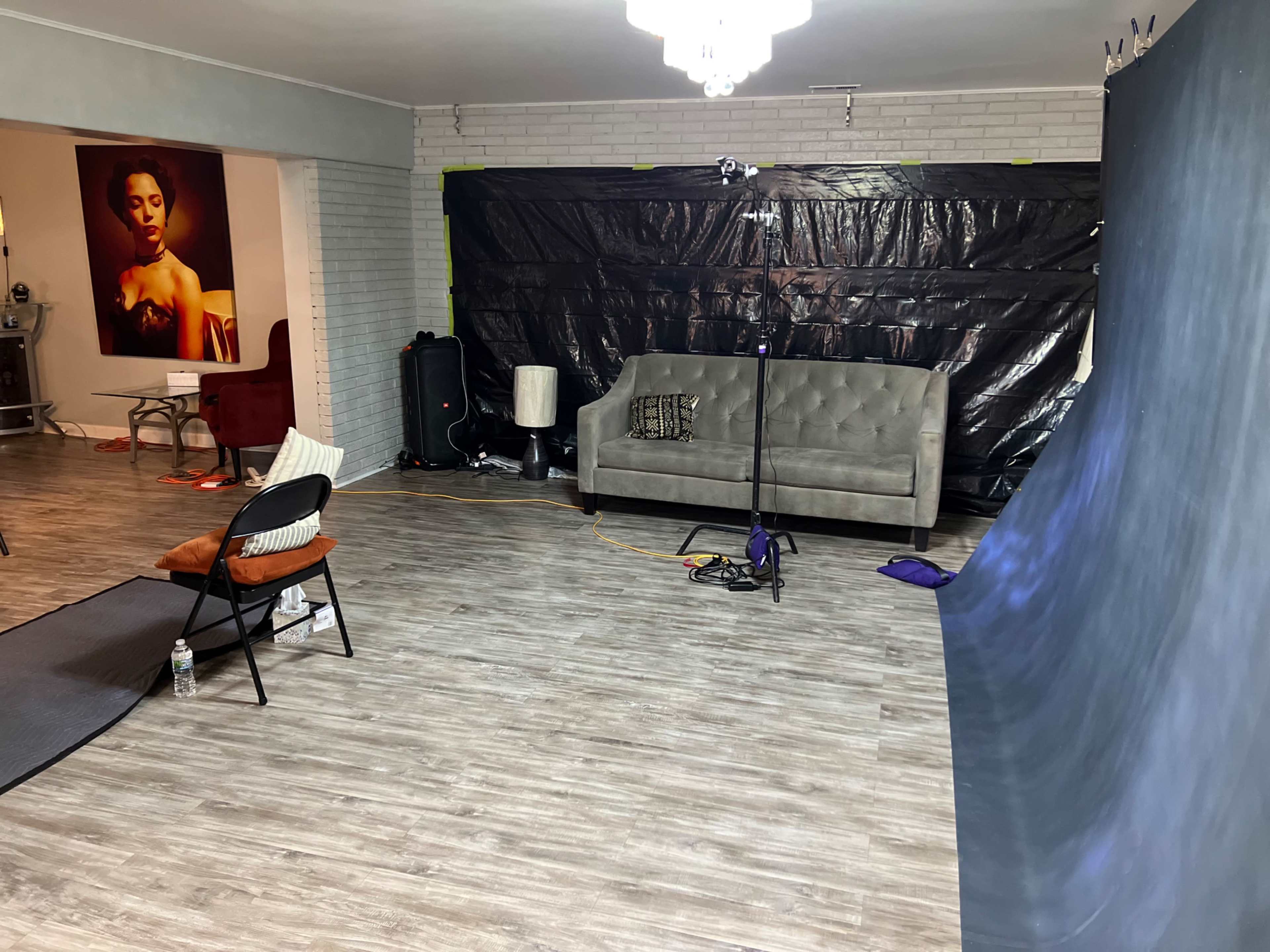 The image shows a spacious room with a gray couch, a black backdrop, and a setup for photography equipment.