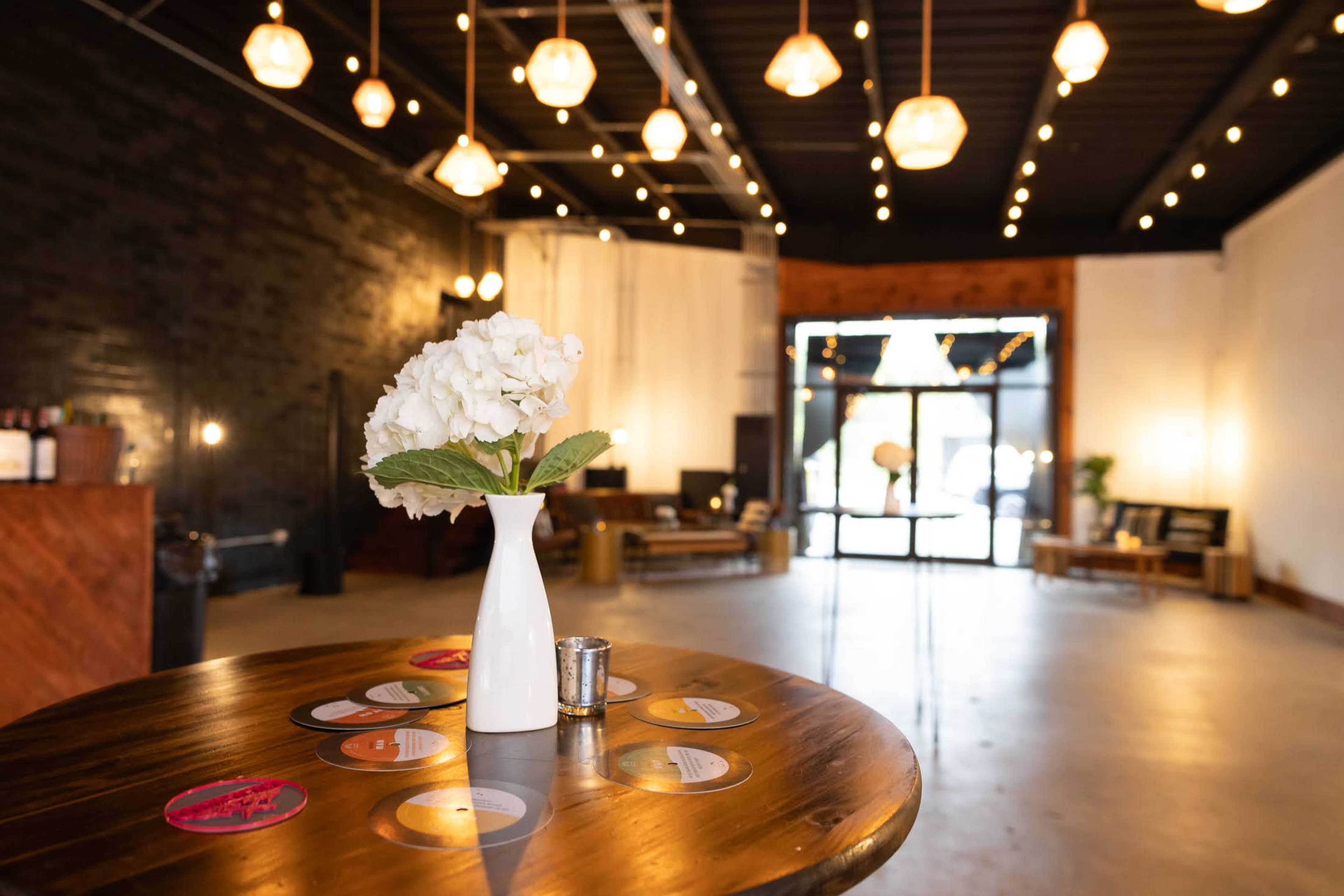 A spacious interior features a table with a vase of flowers and decorative coasters, illuminated by hanging pendant lights.